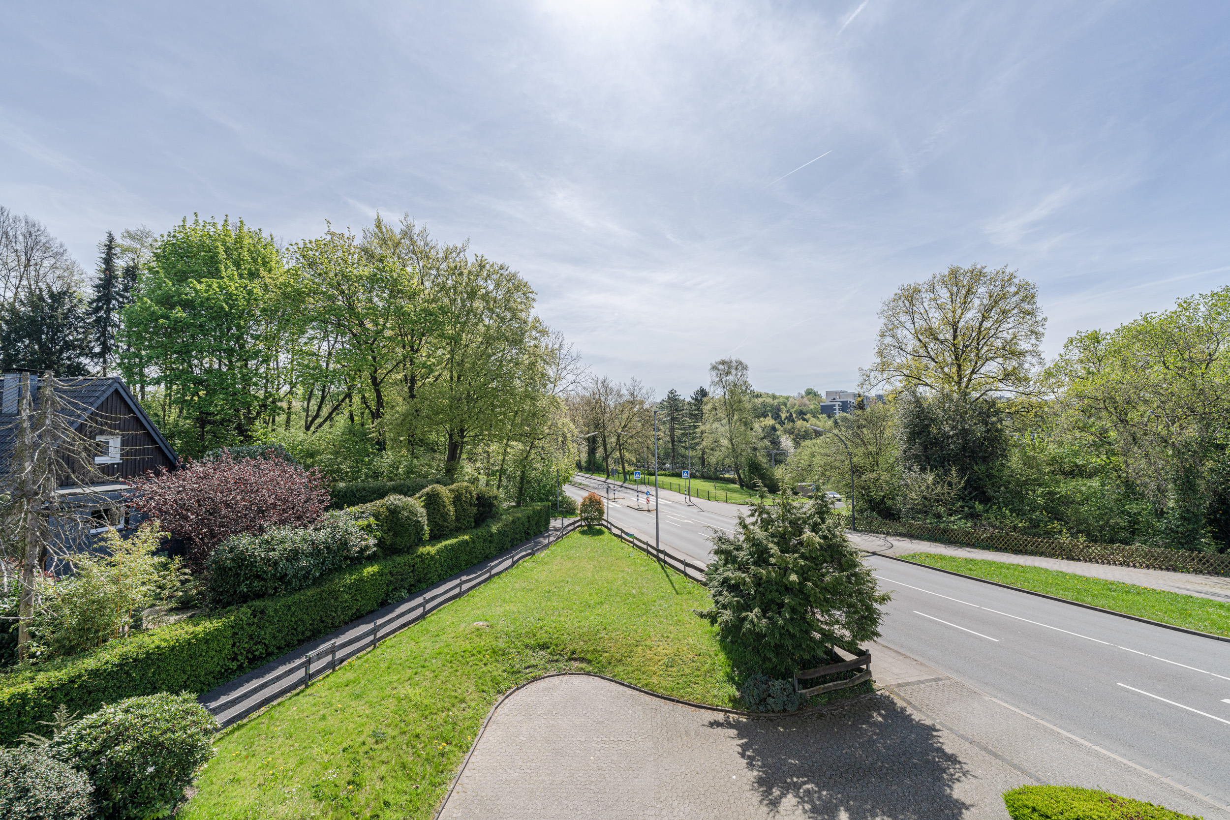 Blick auf eine Straße mit viel Grün, Bäumen und einem Garten am Straßenrand.