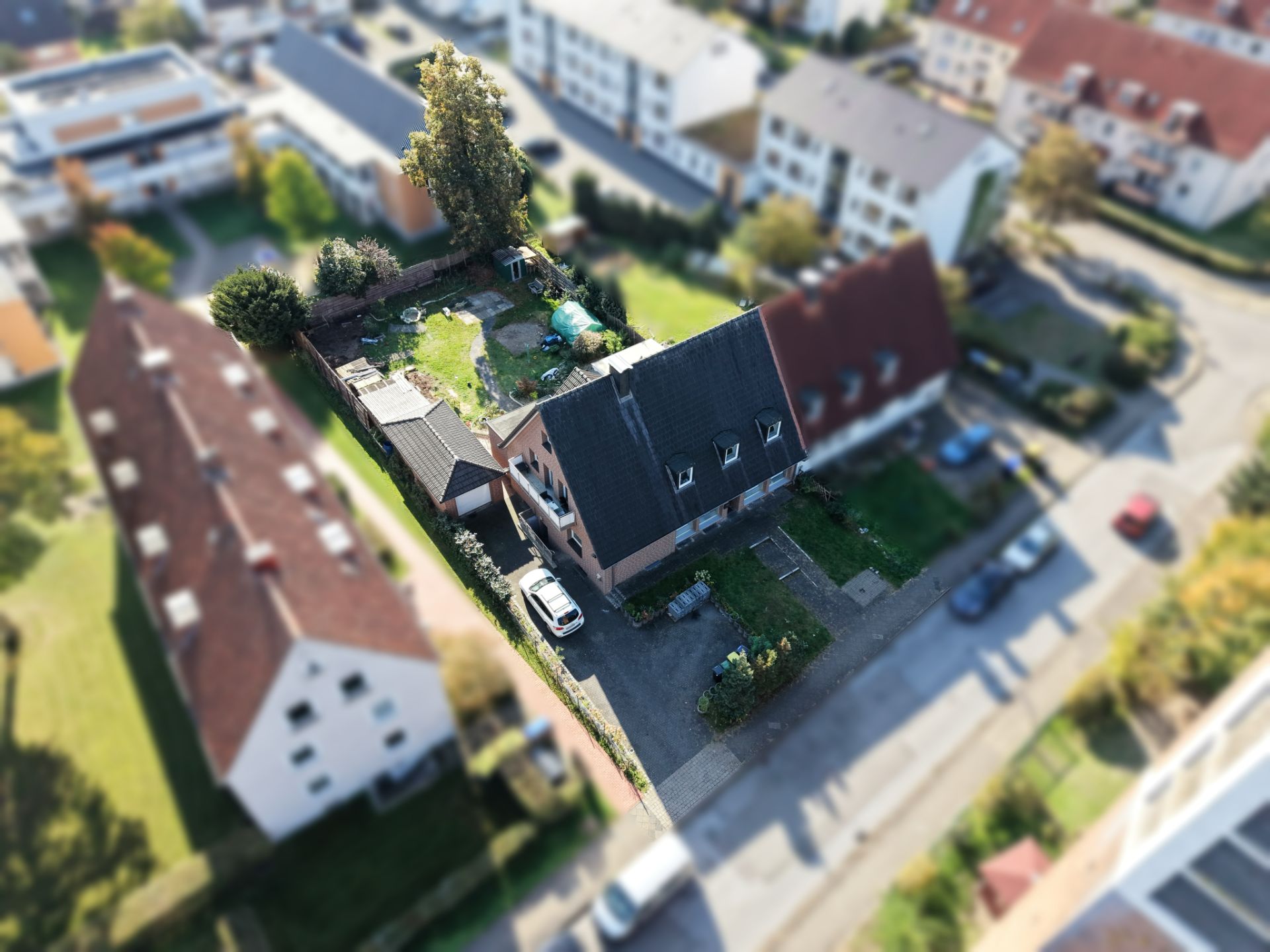 Luftaufnahme eines Wohnhauses mit Garten, Einfahrt und parkendem Auto in einer Wohngegend.