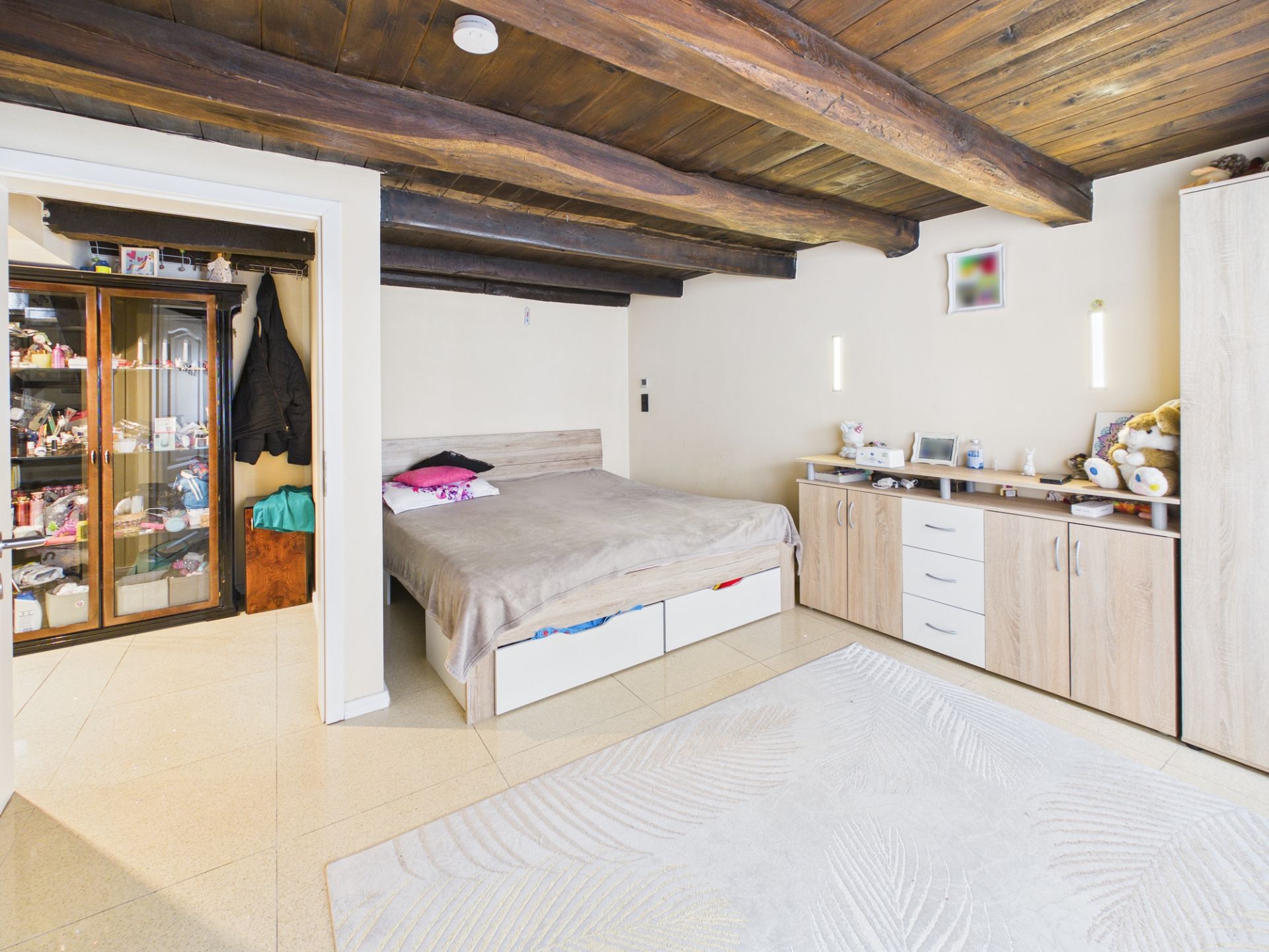 Gemütliches Schlafzimmer mit Holzbalkendecke, Doppelbett, Schrankwand und Teppich.