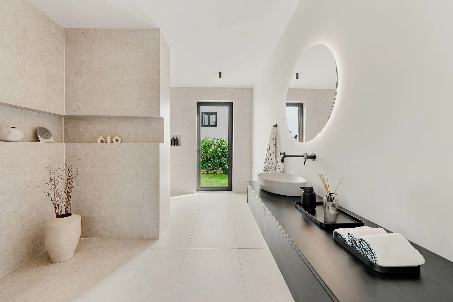 Modernes Badezimmer mit rundem Spiegel, Waschbecken und großer Tür zum Garten.