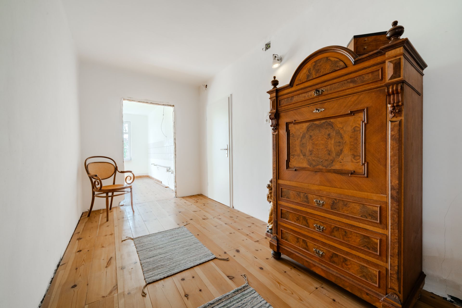 Heller Flur mit Holzschrank, Stuhl und zwei Teppichen auf Holzboden.