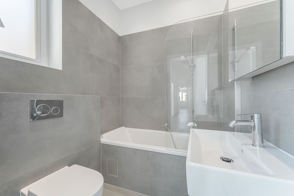 Modernes Badezimmer mit grauen Fliesen, Badewanne, Dusche, WC und Waschbecken.