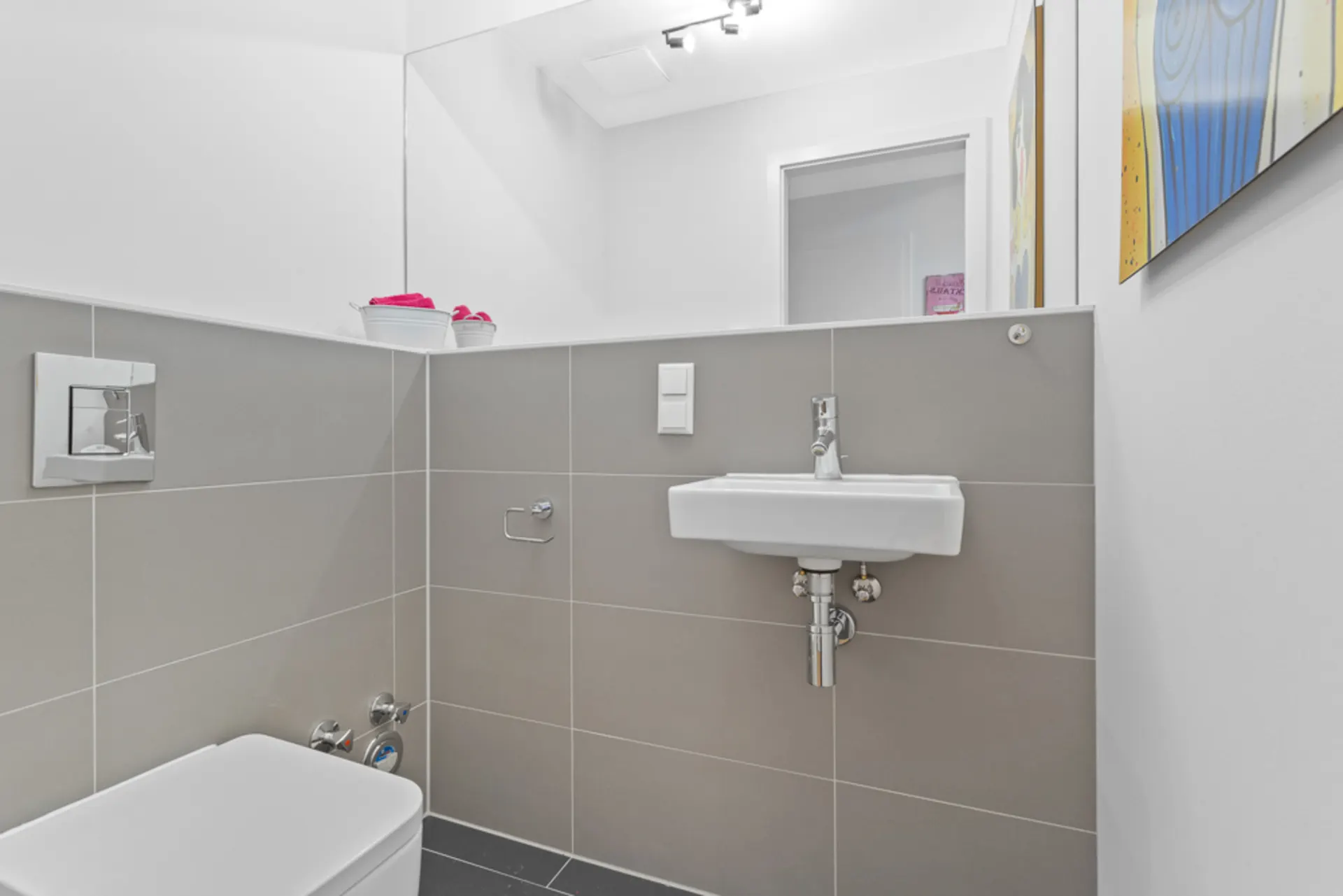 Modernes Gäste-WC mit grauen Fliesen, Wandtoilette, Waschbecken und Wandbild.