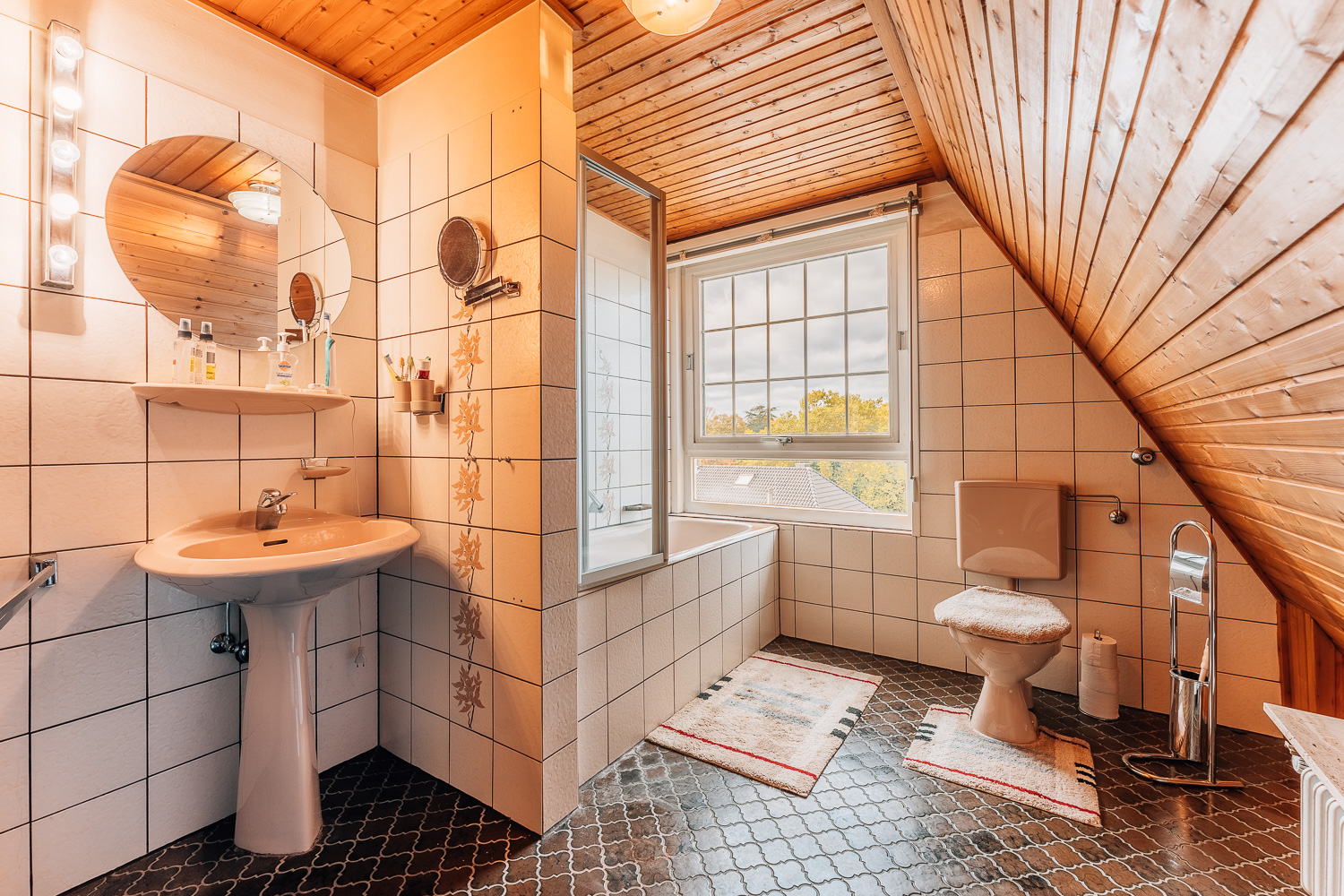 Badezimmer mit Waschbecken, Spiegel, Badewanne, WC und großem Fenster unter Dachschräge.