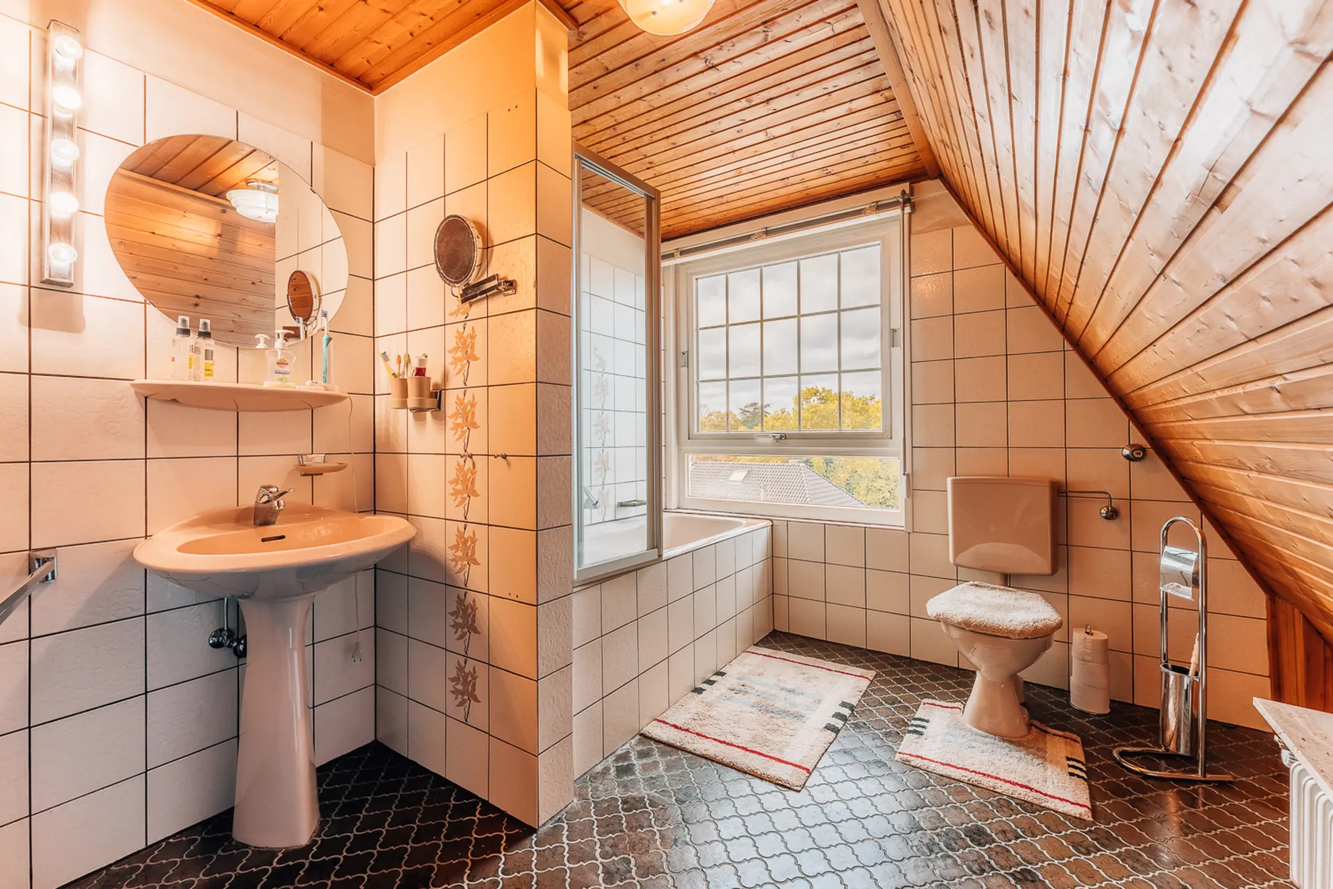 Badezimmer mit Waschbecken, Spiegel, Badewanne, WC und großem Fenster unter Dachschräge.