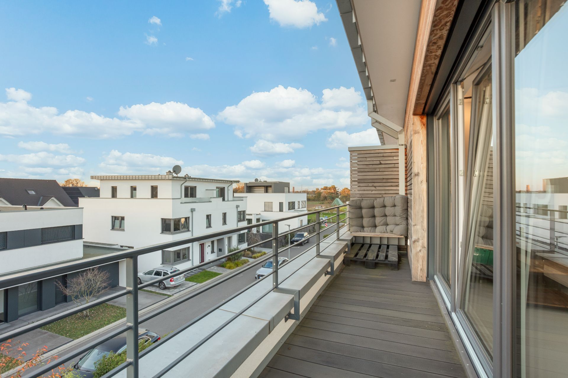 Moderner Balkon mit Sitzbank und Blick auf eine Wohnstraße mit weißen Häusern.