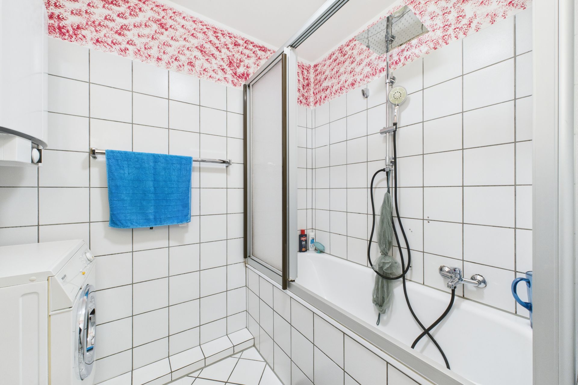 Badezimmer mit Badewanne, Duschwand, weiß gefliesten Wänden und blauem Handtuch.