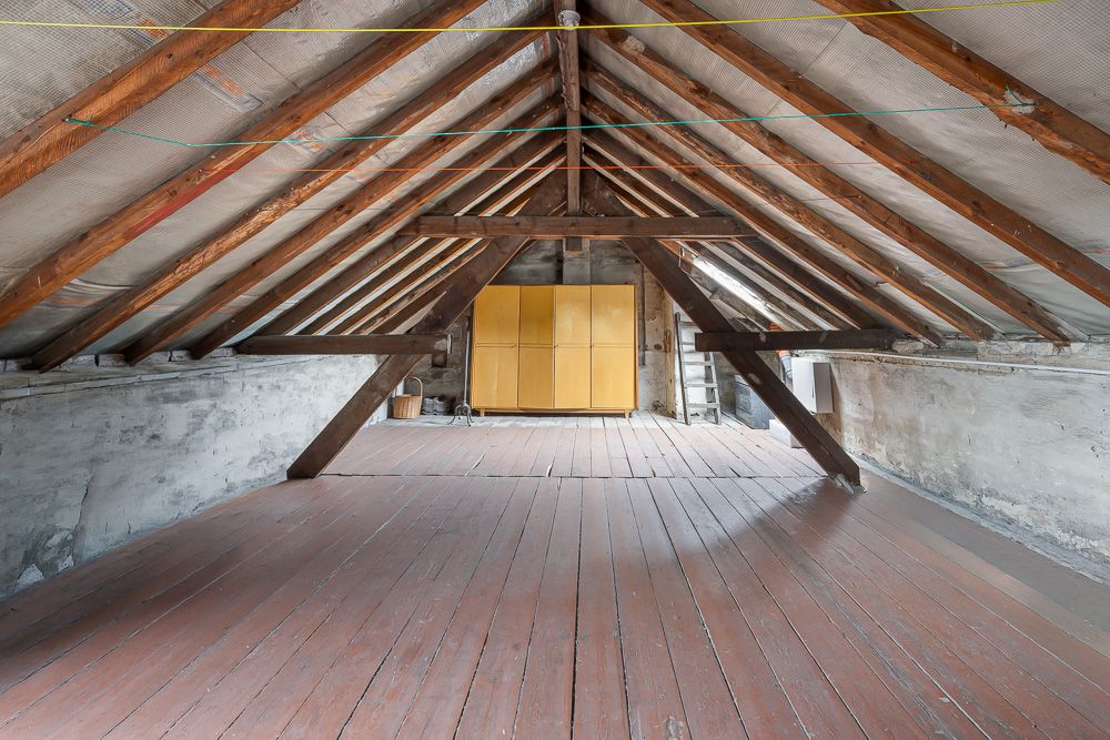 Dachboden mit sichtbaren Holzbalken, Holzfußboden und gelbem Schrank im Hintergrund.