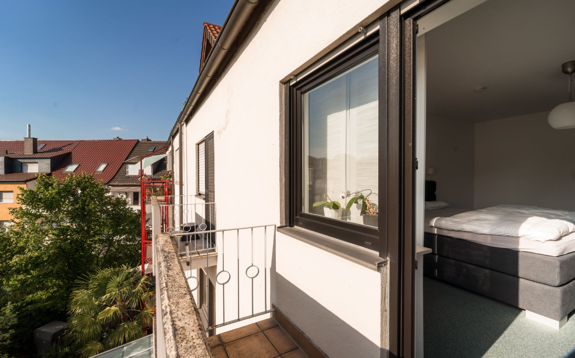 Balkon mit Blick auf Bäume, angrenzendes Schlafzimmer mit Bett und Fenster.