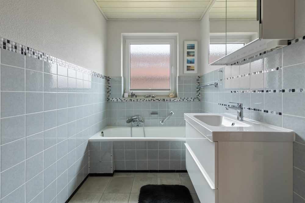 Modernes Badezimmer mit Badewanne, Waschbecken und hellblauen Fliesen.