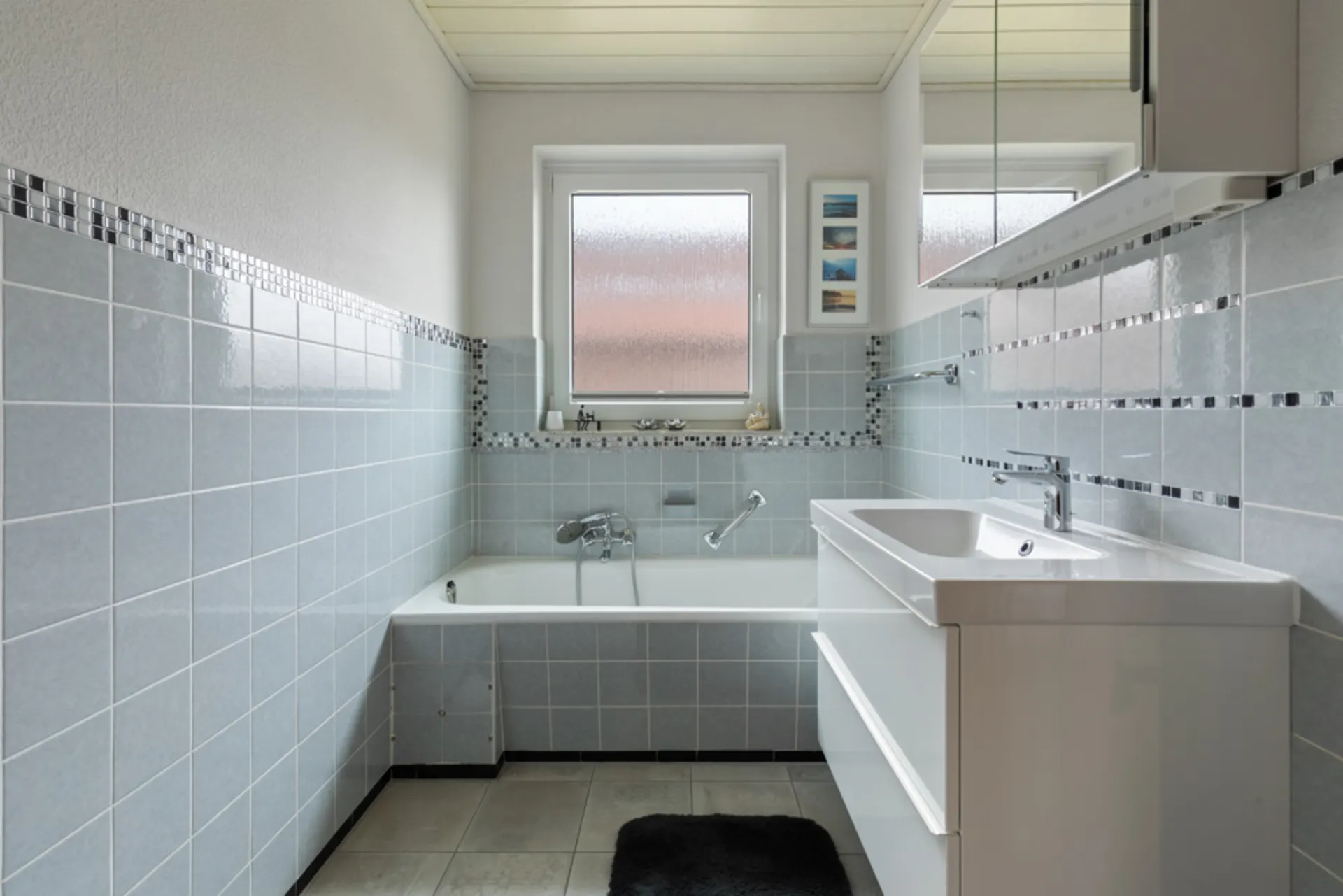 Modernes Badezimmer mit Badewanne, Waschbecken und hellblauen Fliesen.