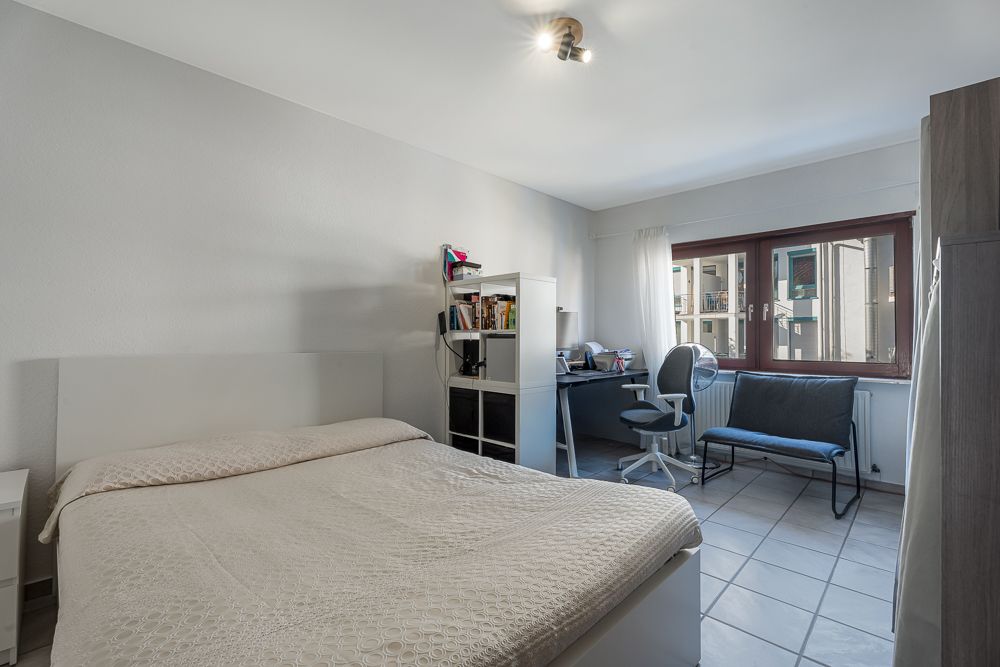 Helles Schlafzimmer mit Bett, Regal, Schreibtisch, Stuhl und großem Fenster.