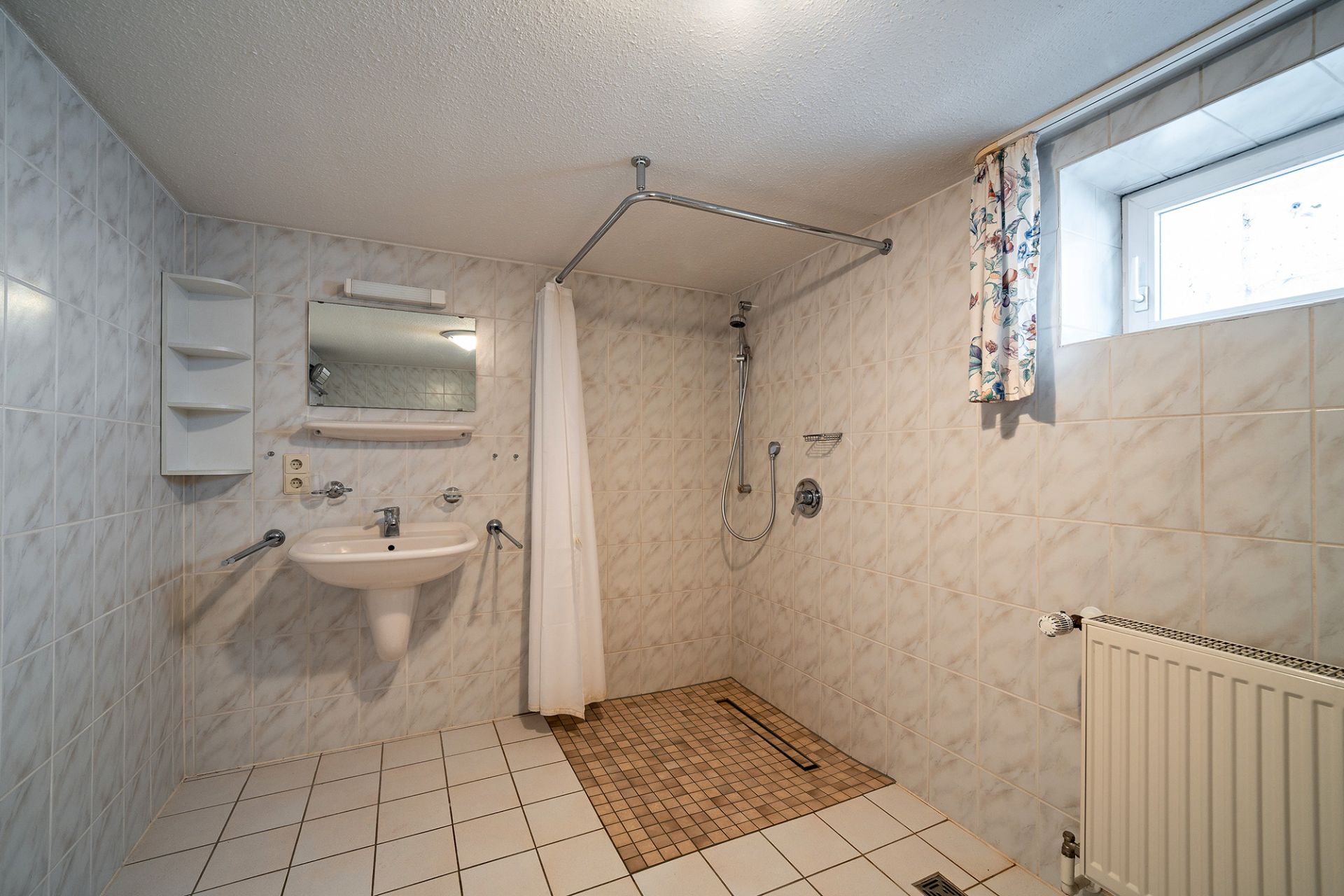 Barrierefreies Badezimmer mit bodengleicher Dusche, Waschbecken, Spiegel und Fenster.