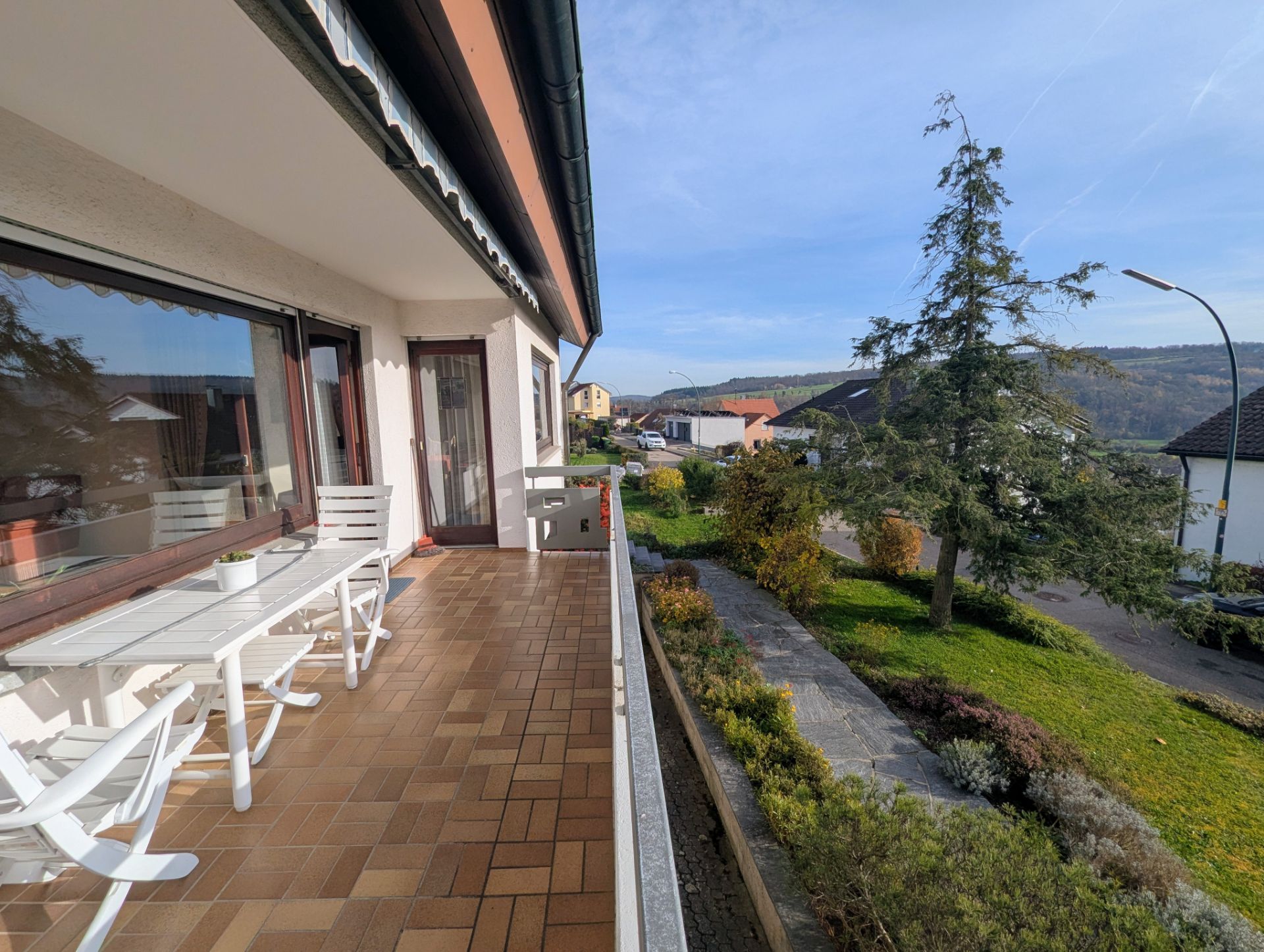 Geräumiger Balkon mit weißen Gartenmöbeln und Blick auf Garten und Wohnstraße.
