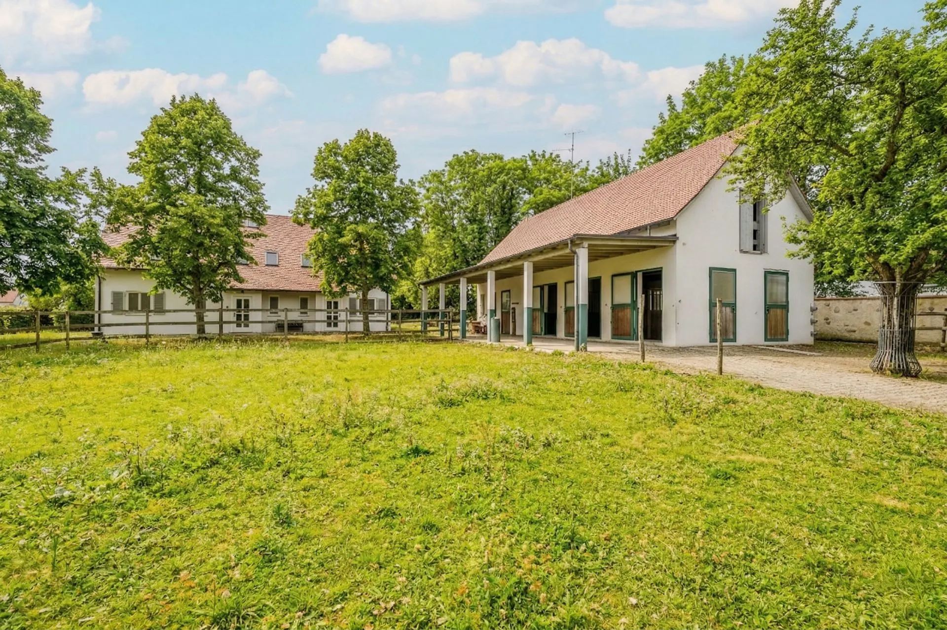 Zwei Wohngebäude mit Garten und Bäumen bei sonnigem Wetter.