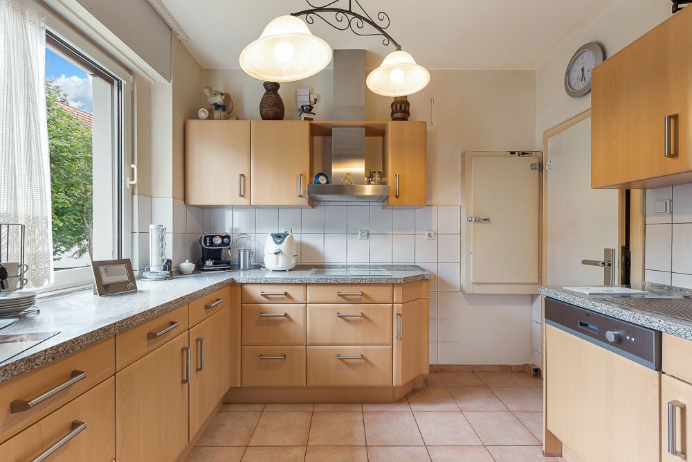 Helle Küche mit Holzschränken, großen Fenstern und modernen Geräten.