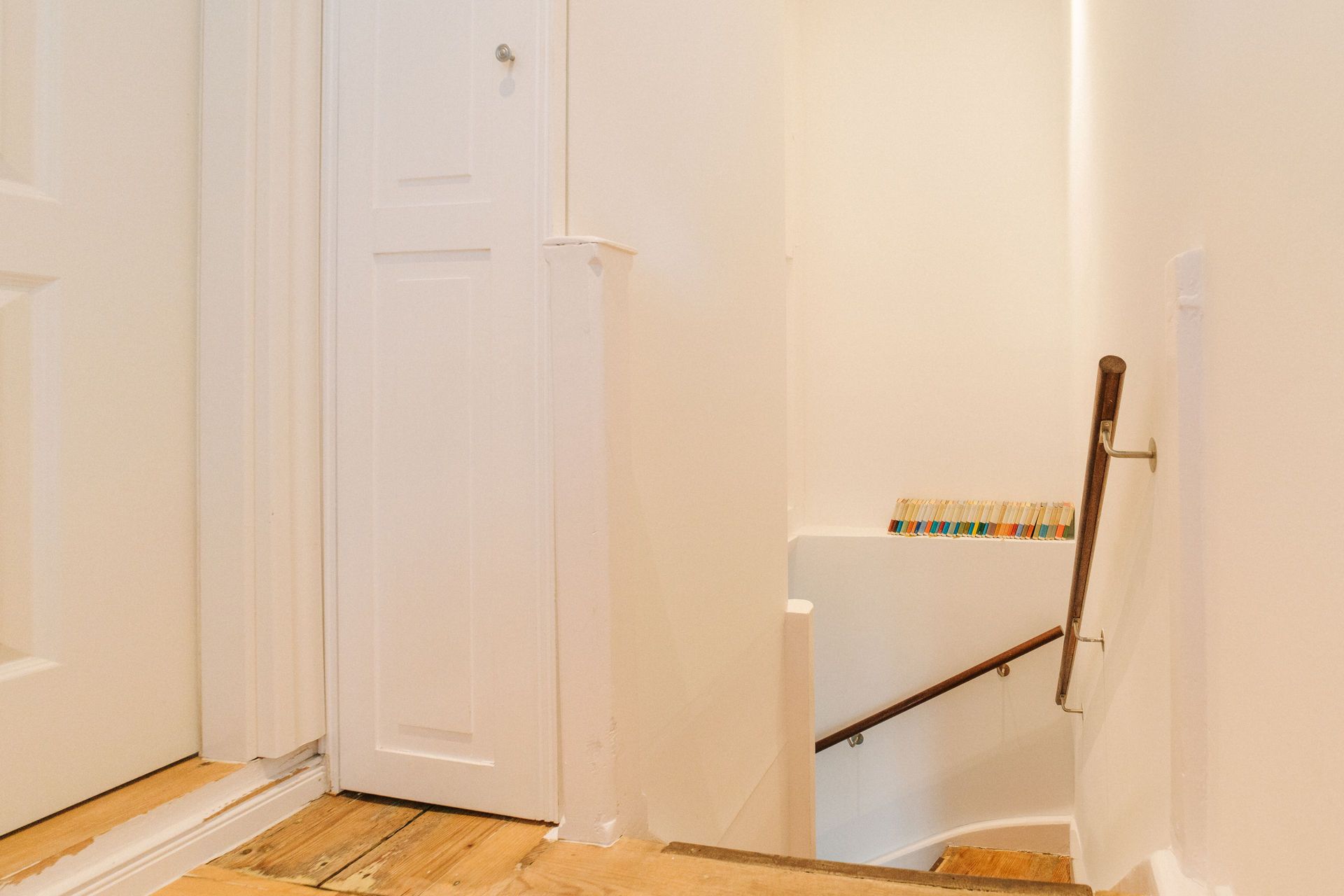 Heller Flur mit Holzboden, Treppe mit Handlauf und Regal mit Büchern an der Wand.