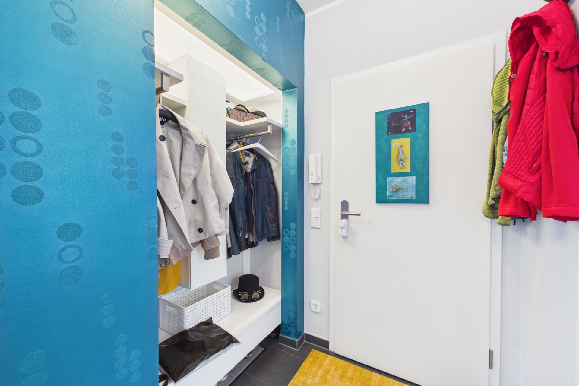 Eingangsbereich mit Garderobe, Jacken, Hüten und bunten Wänden.