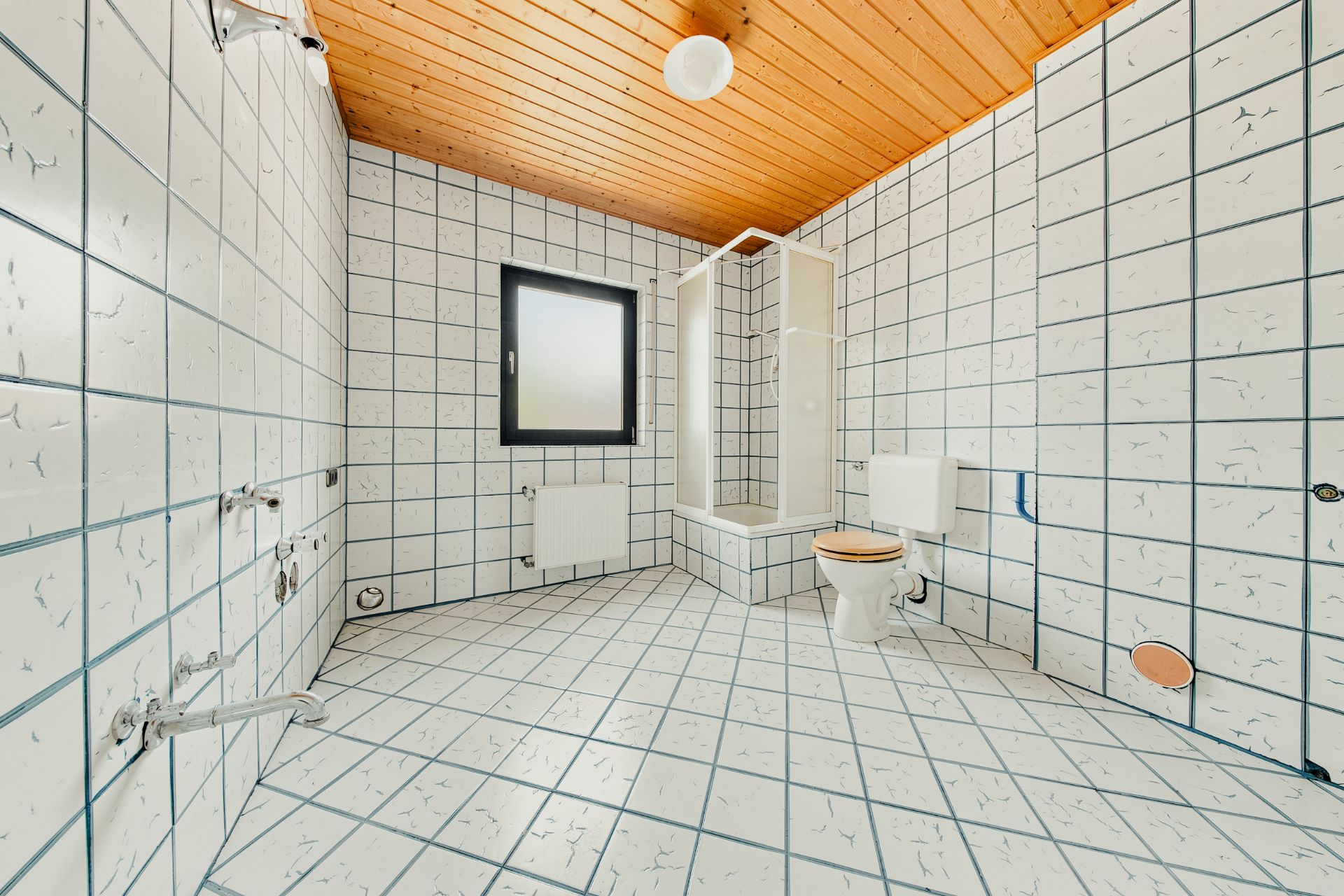 Helles Badezimmer mit weißen Fliesen, Dusche, WC, Fenster und Holzdecke.