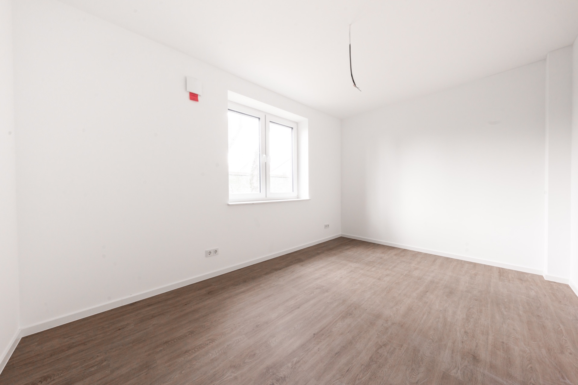 Leerer Raum mit weiß gestrichenen Wänden, Fenster und Holzfußboden.
