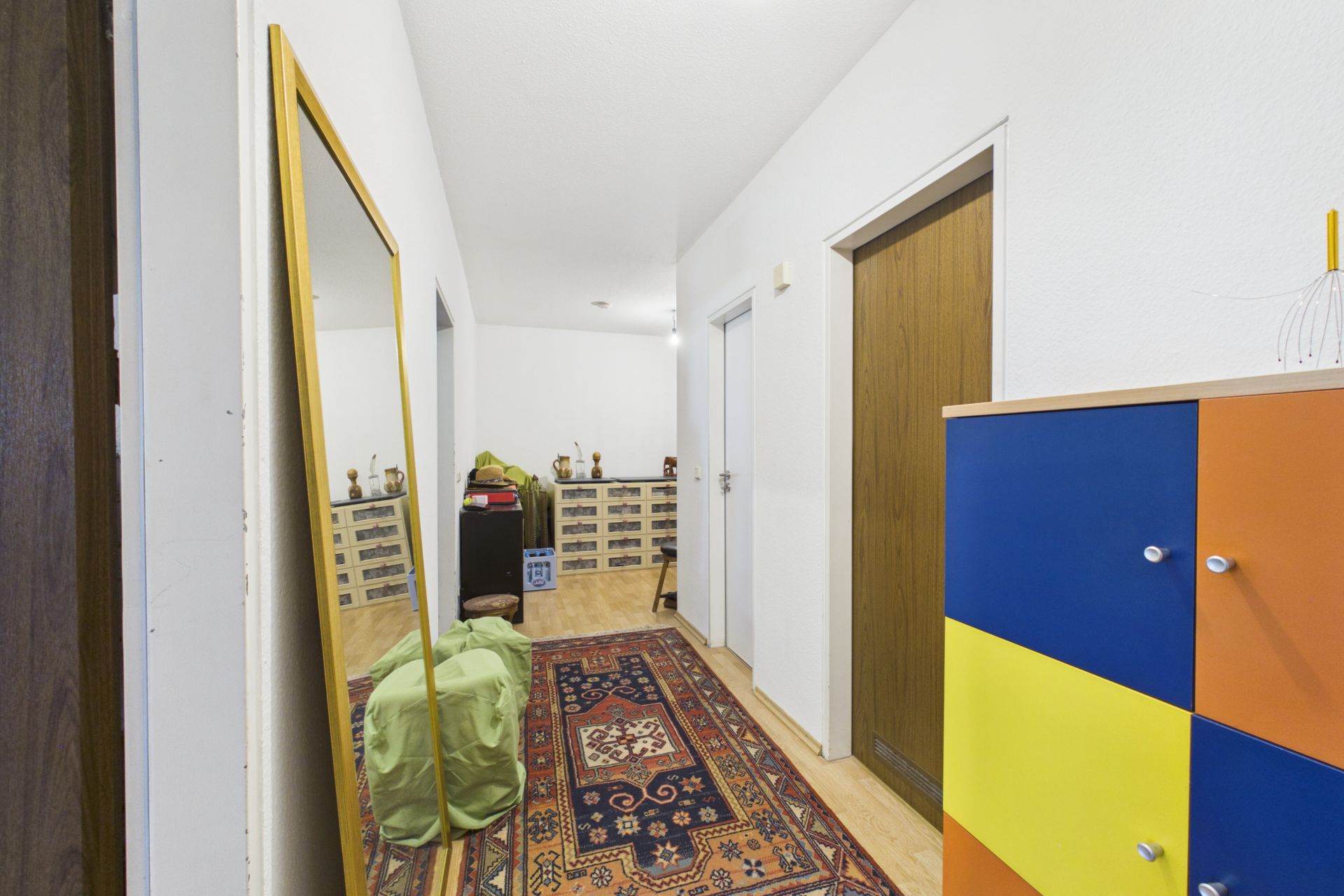 Flur mit buntem Schrank, großem Spiegel und Teppich auf Holzboden.
