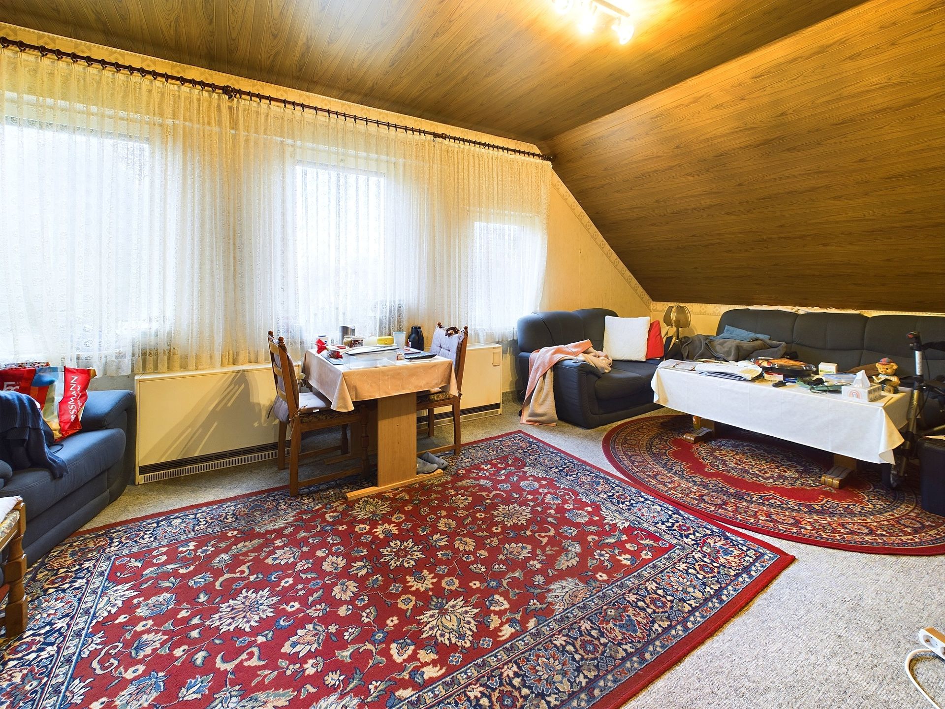 Gemütliches Wohnzimmer mit Sofas, Esstisch, Teppichen und Holzdecke.