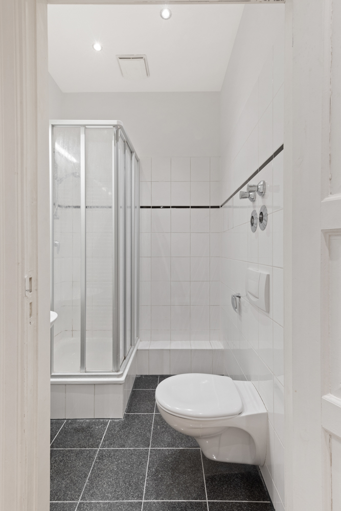 Modernes Bad mit Duschkabine, Wandtoilette und schwarzen Bodenfliesen.
