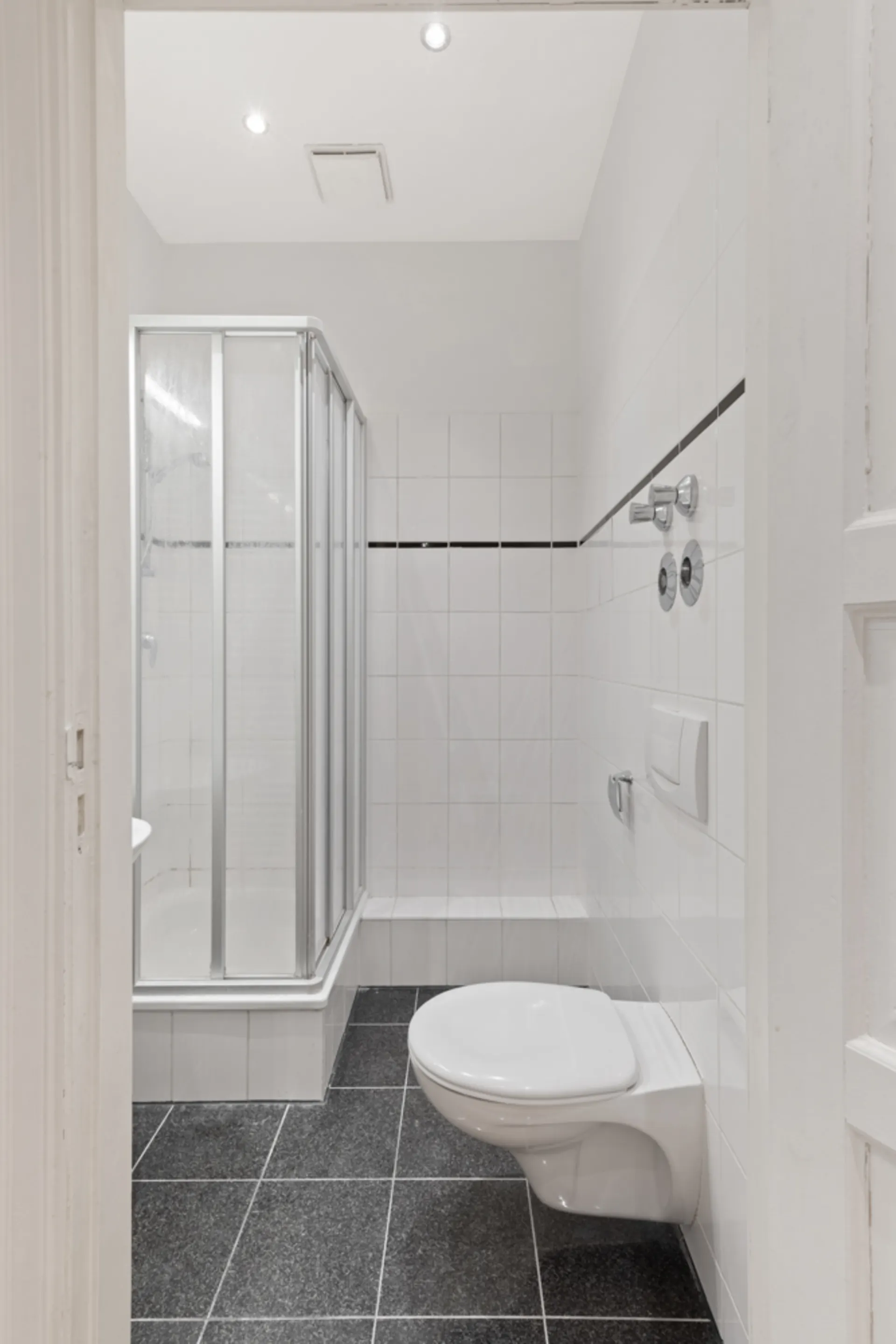 Modernes Bad mit Duschkabine, Wandtoilette und schwarzen Bodenfliesen.