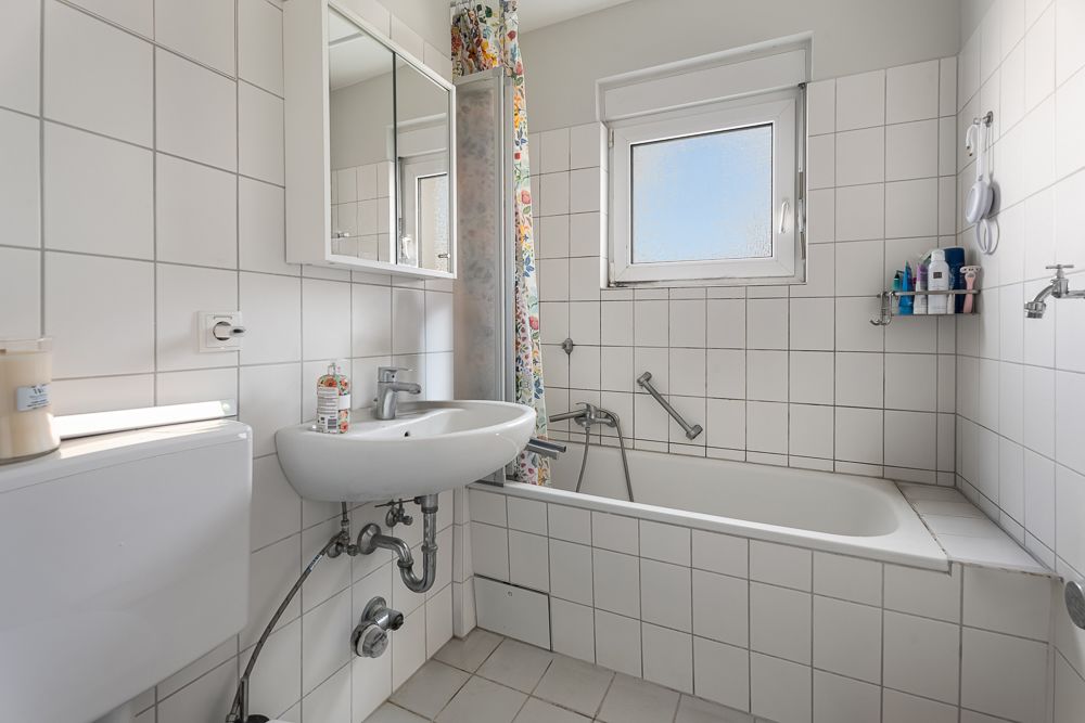 Helles Badezimmer mit Badewanne, Waschbecken, Spiegel und Fenster.