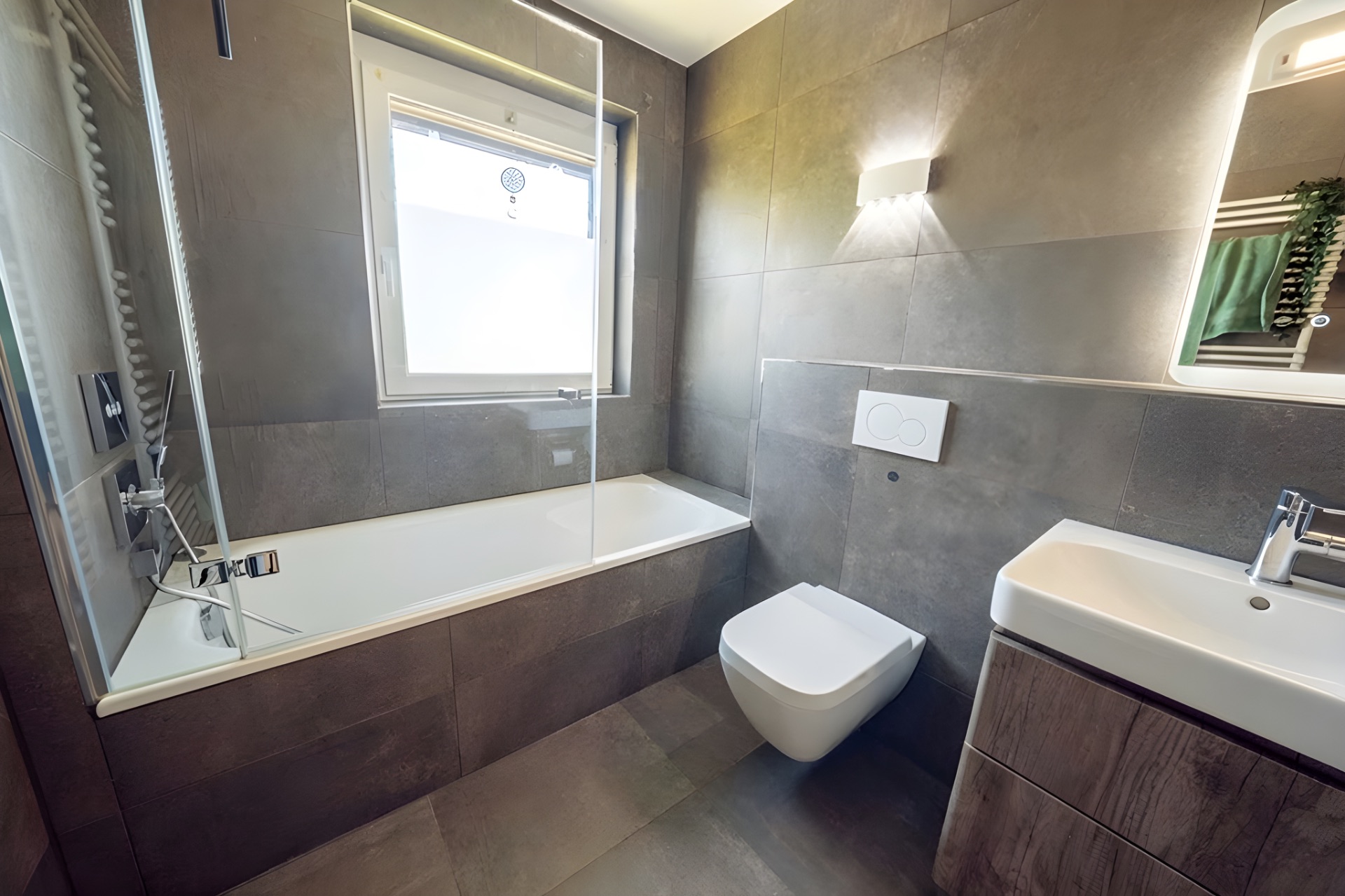 Modernes Badezimmer mit Badewanne, Wandtoilette, Waschbecken und Fenster.