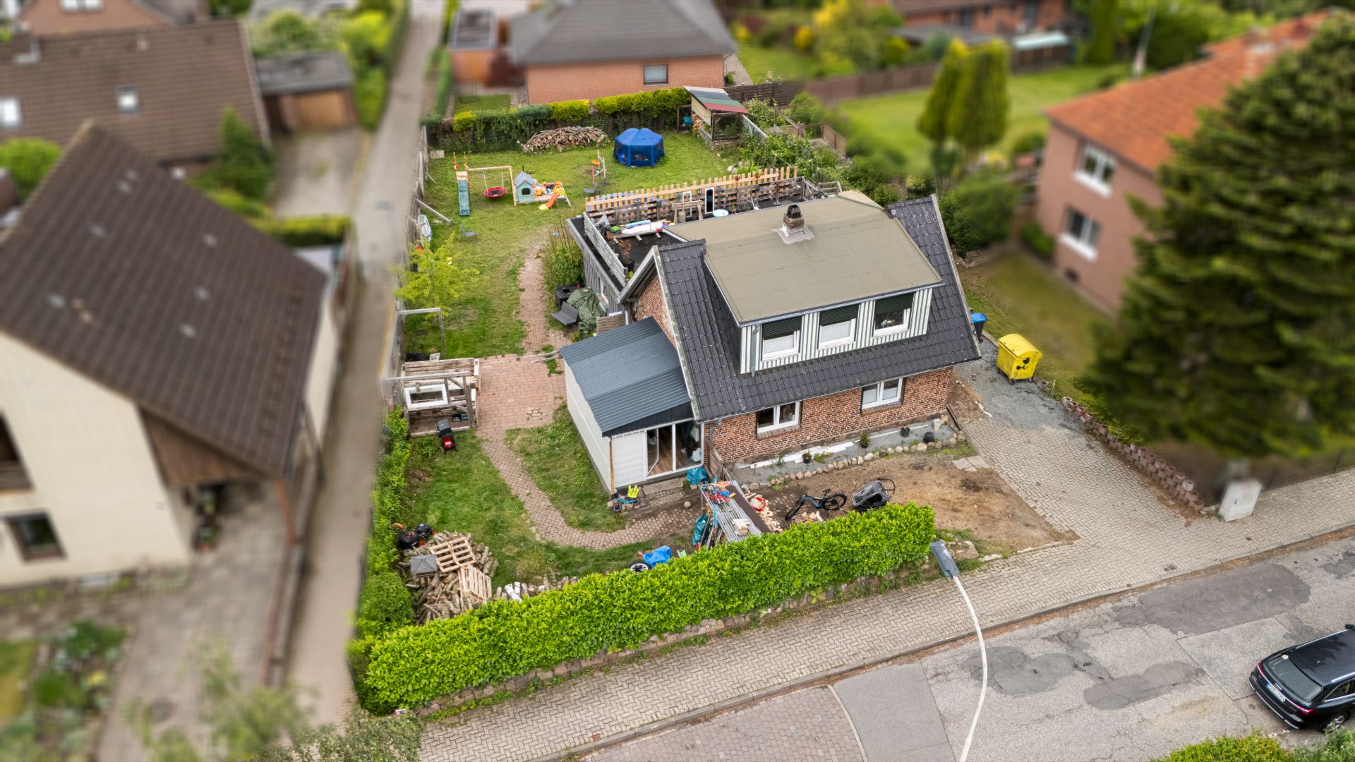 Luftaufnahme eines Einfamilienhauses mit Garten, umgeben von Hecken und Nachbarhäusern.