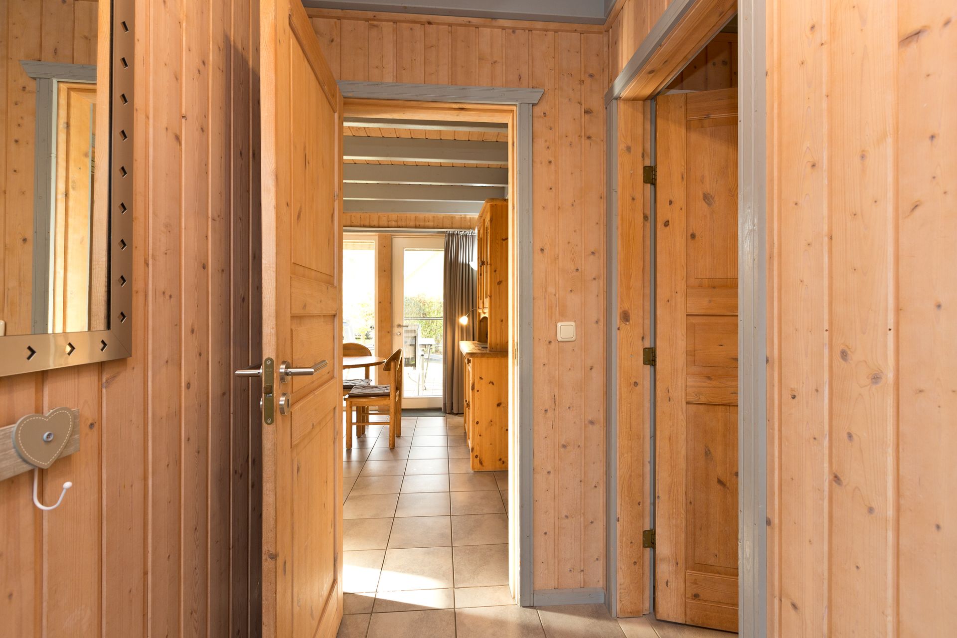 Flur mit Holzwänden, offene Türen, Blick ins Esszimmer mit Tisch und Stühlen.