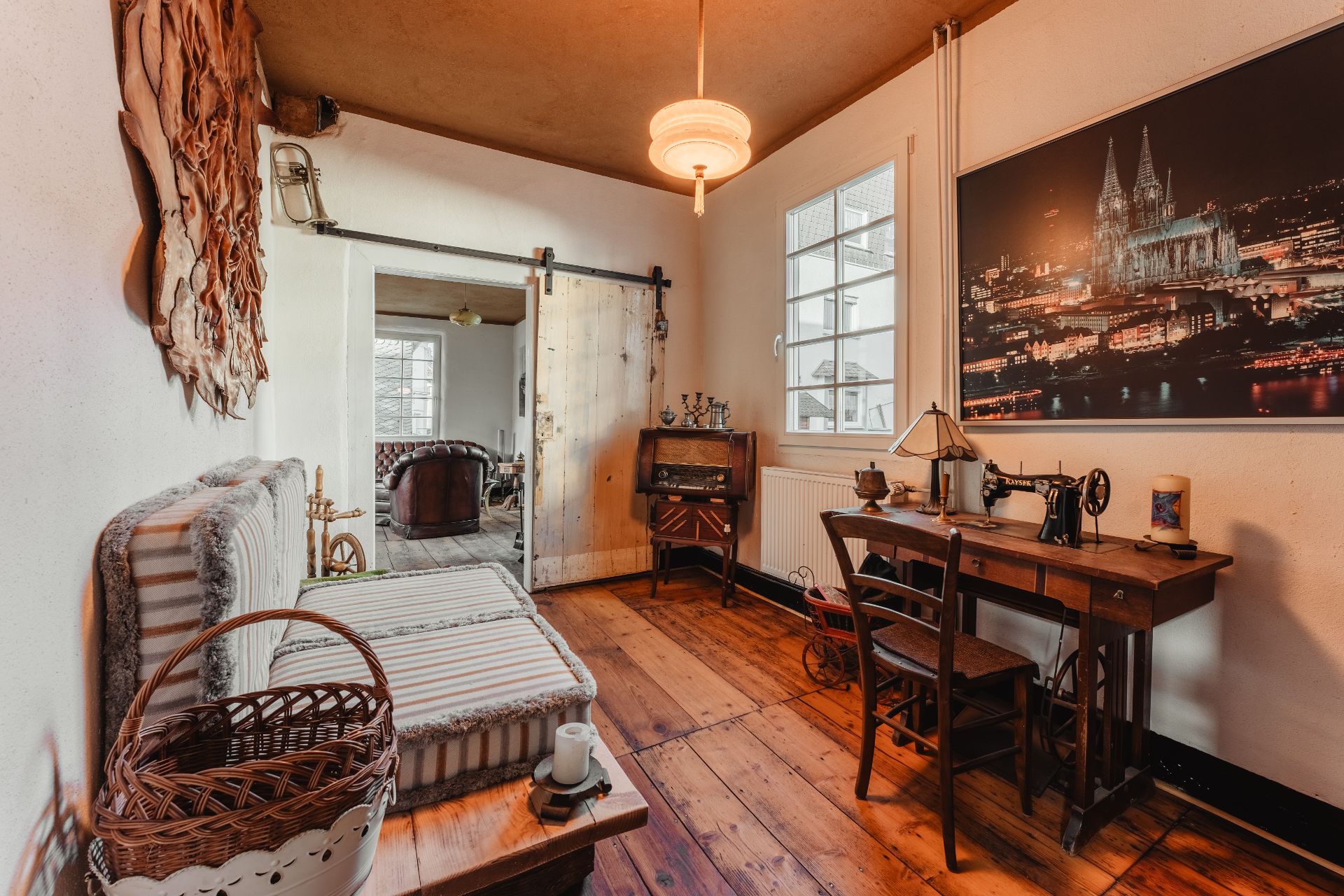 Gemütliches Zimmer mit Holzboden, Nähmaschine auf Schreibtisch, Sitzbank und großem Foto an der Wand.