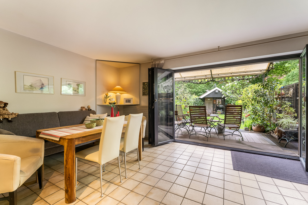 Wohnzimmer mit Esstisch, offenen Türen zur Terrasse und Blick in einen grünen Garten.
