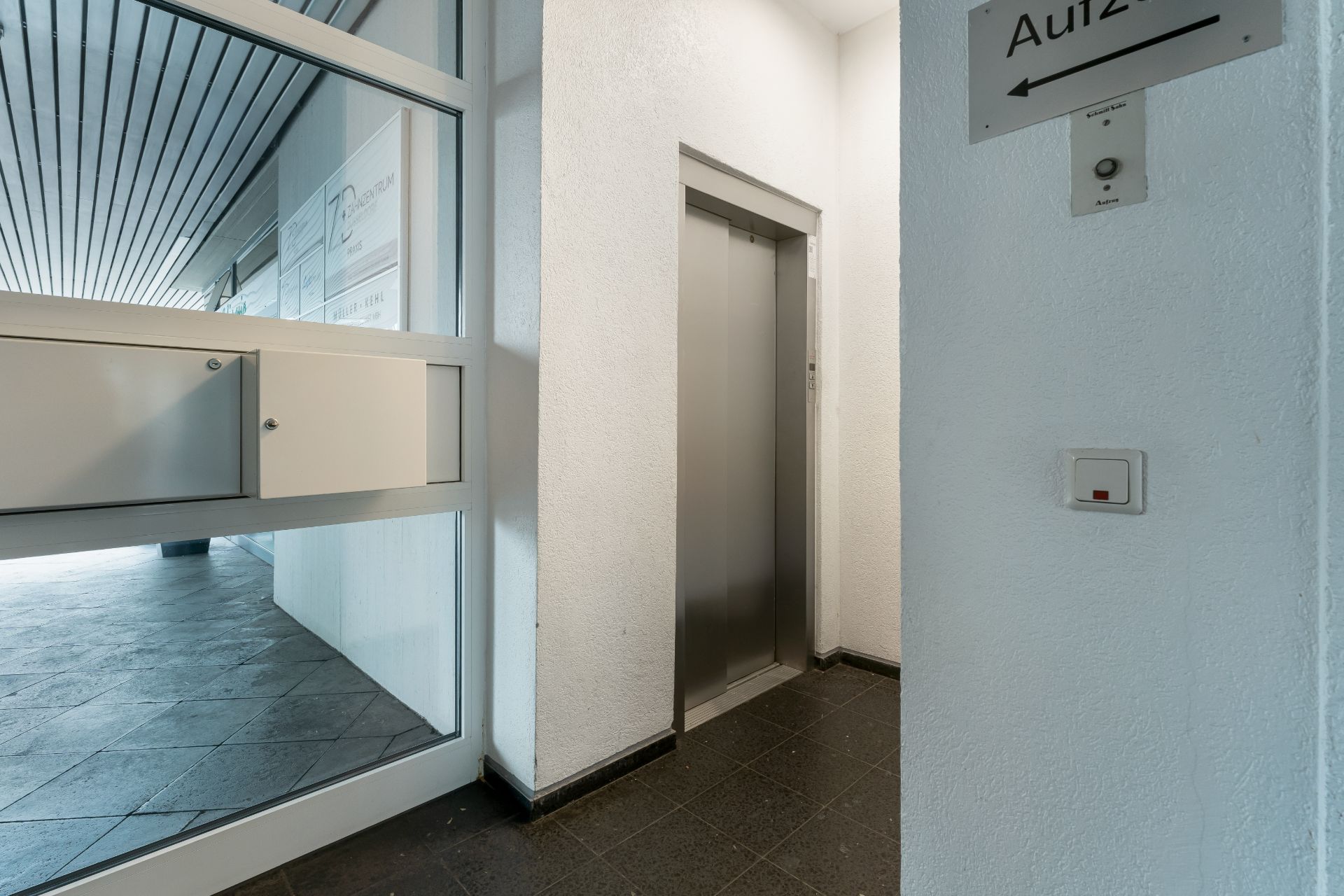 Eingangsbereich mit Aufzug und Briefkästen neben einer Glastür.