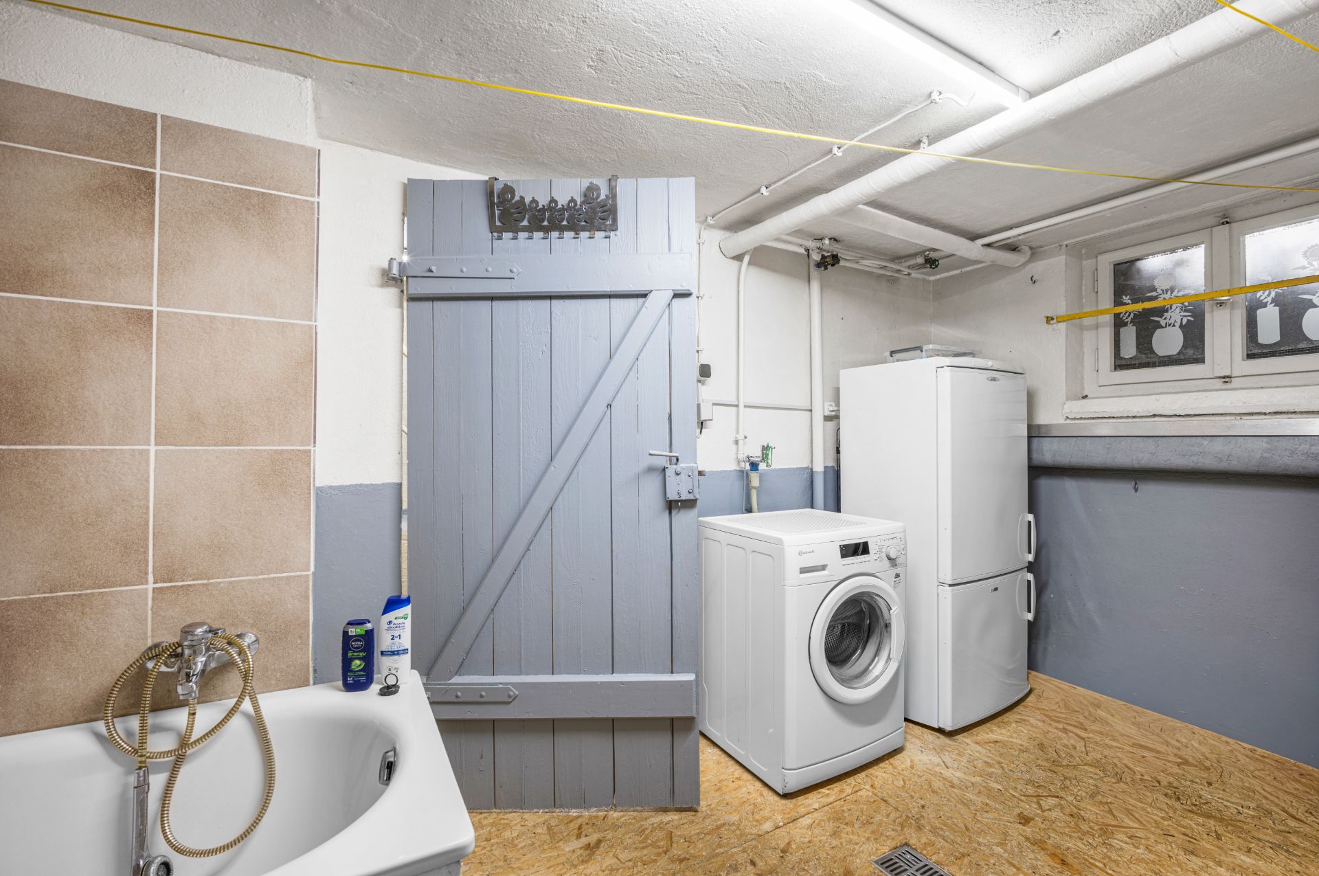 Waschraum mit Badewanne, Waschmaschine, Kühlschrank und Fenster.