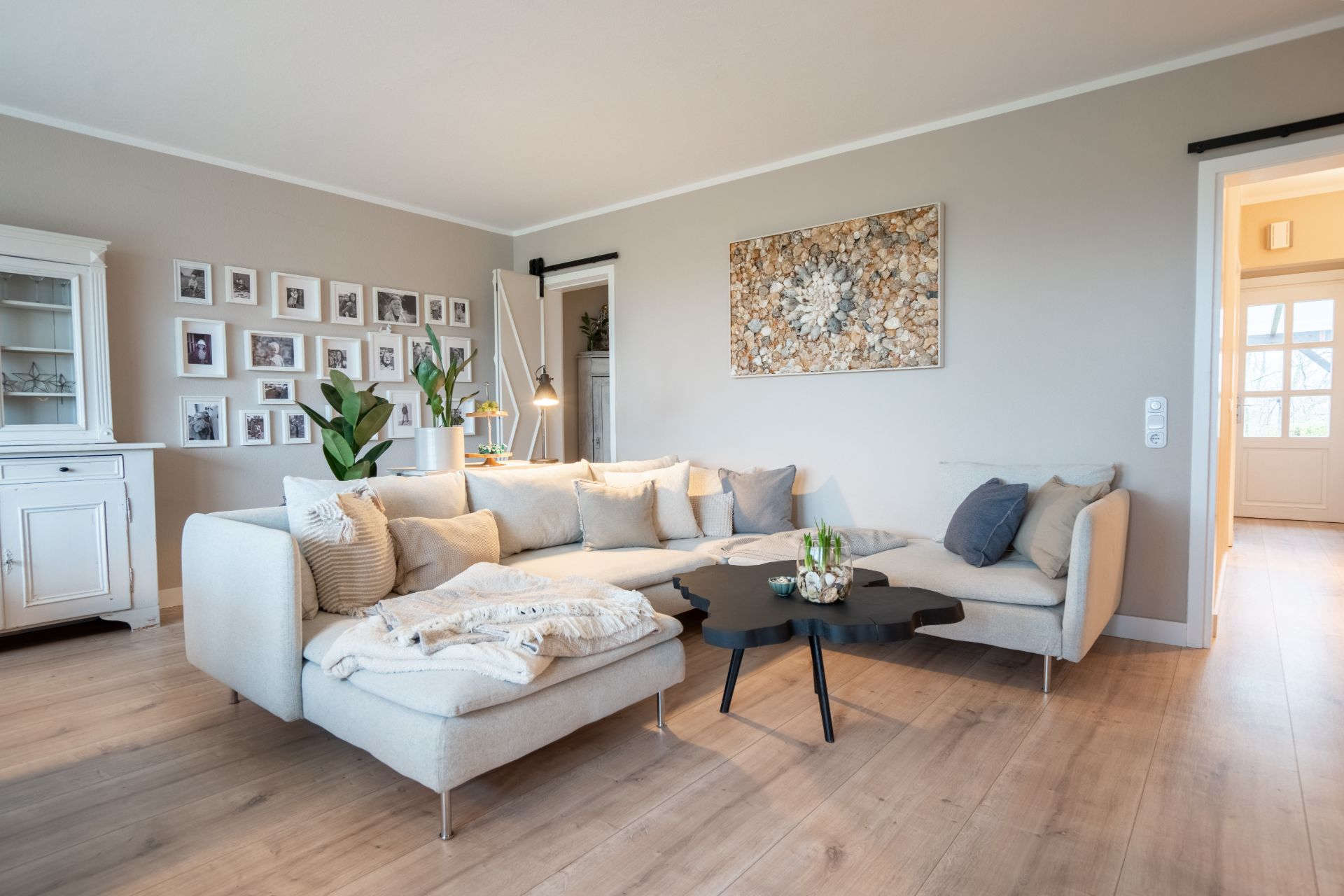 Helles Wohnzimmer mit großer Eckcouch, Couchtisch und vielen Bildern an der Wand.