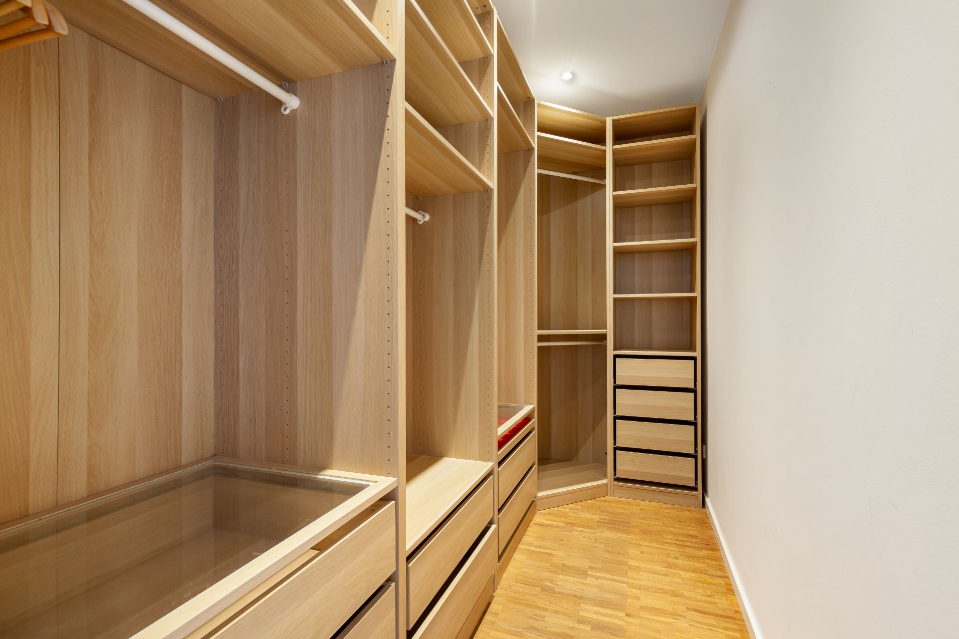 Begehbarer Kleiderschrank mit Holzregalen und Schubladen, leer und gut beleuchtet.
