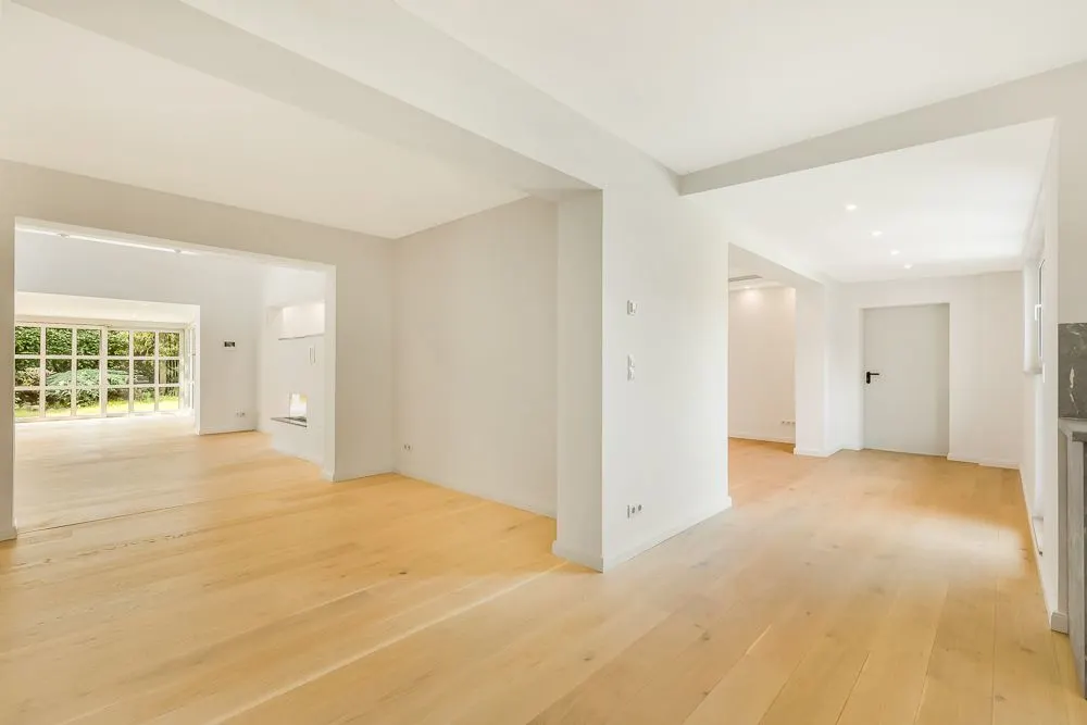 Helles, leeres Zimmer mit Holzboden und großen Fenstern zum Garten.