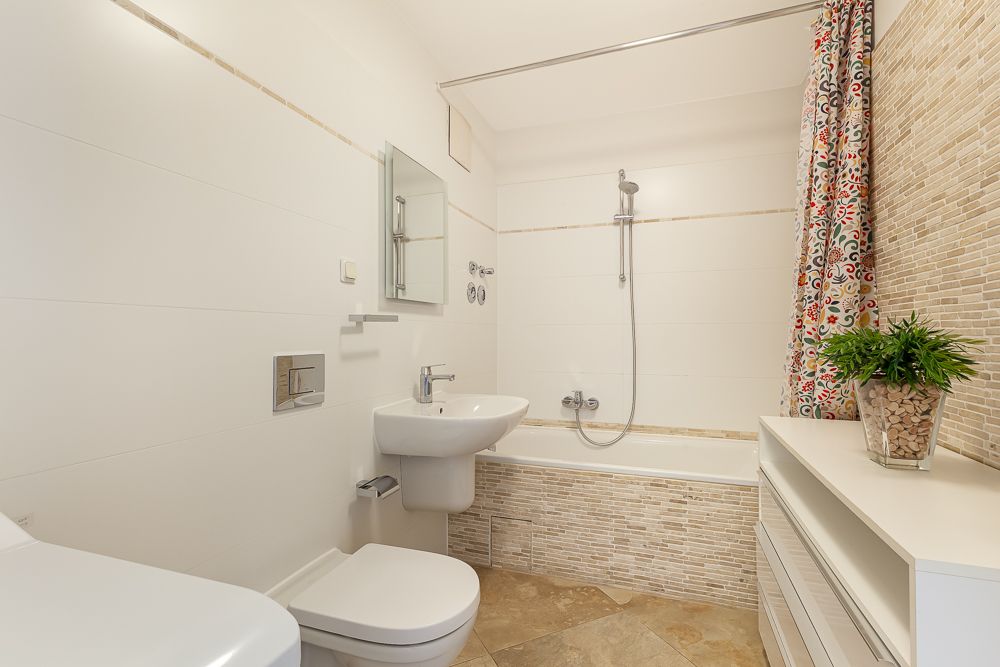 Helles Badezimmer mit Badewanne, Waschbecken, WC, Spiegel und bunter Duschvorhang.