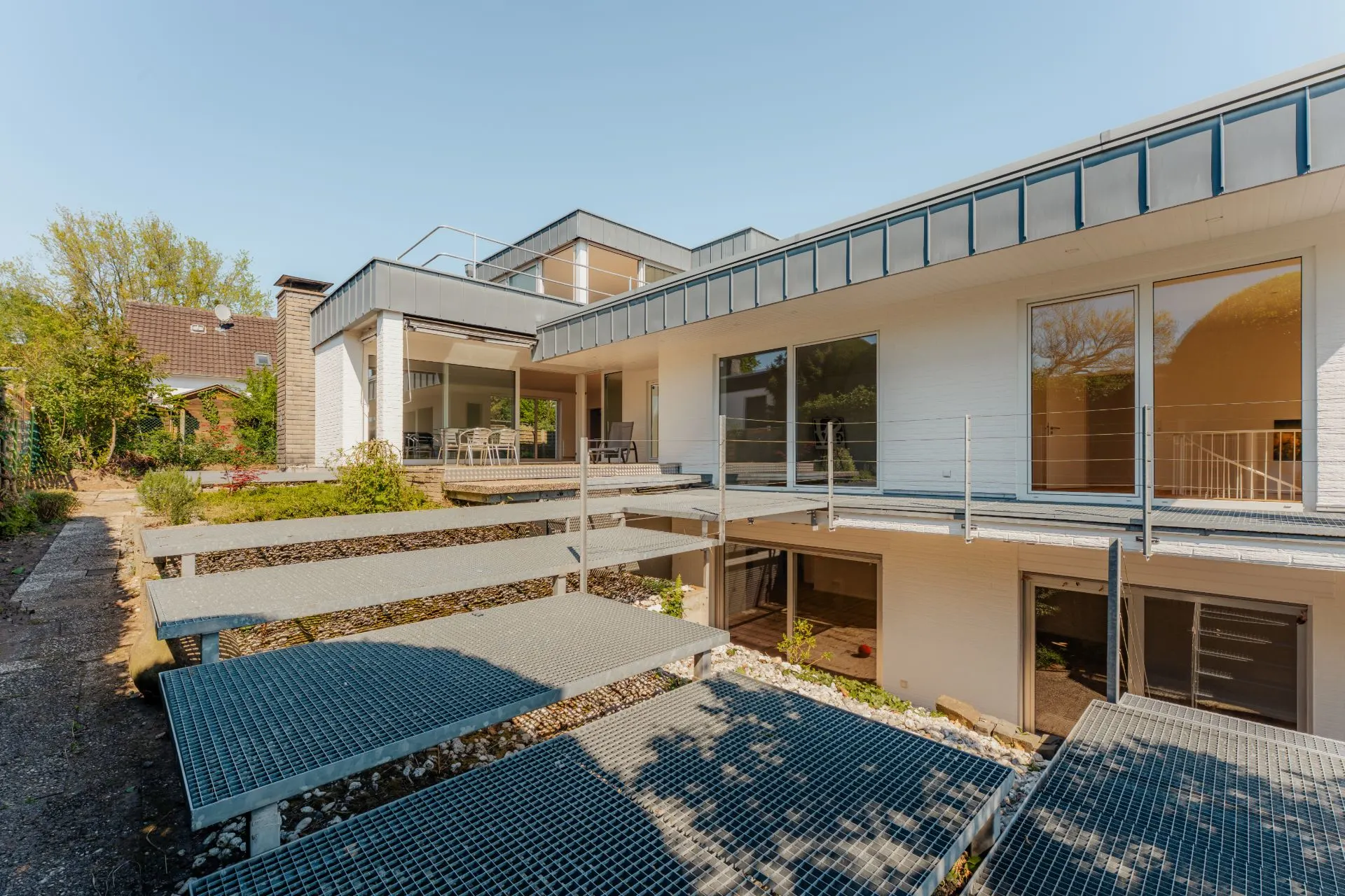 Modernes Wohnhaus mit großen Fenstern, Terrasse und Metallstegen im Garten.