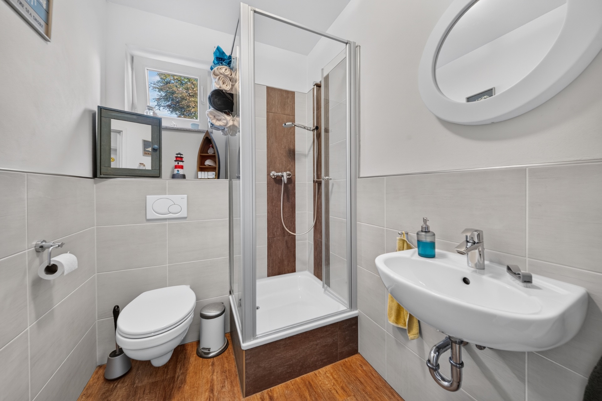 Modernes Badezimmer mit Dusche, WC, Waschbecken und Spiegel, helle Fliesen und Holzfußboden.