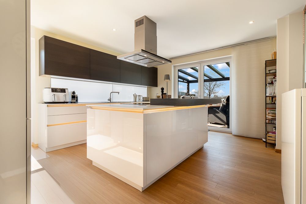 Moderne Küche mit Kochinsel, Holzfußboden und großen Fenstern zu einer Terrasse.