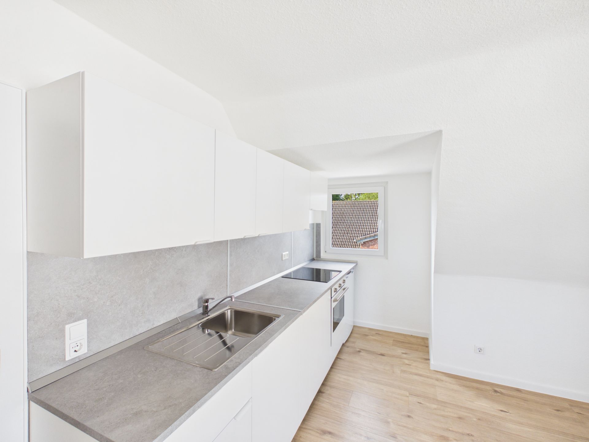 Helle moderne Einbauküche mit weißen Schränken, Spüle und Herd, Holzfußboden und Fenster.
