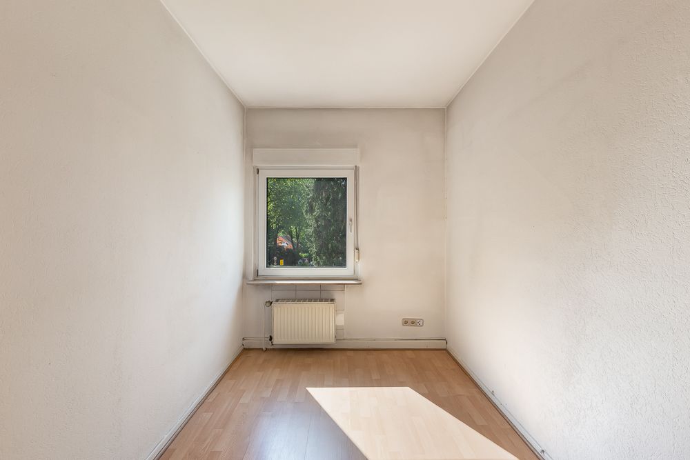 Kleiner leerer Raum mit hellem Laminatboden, Fenster und Heizkörper an der Wand.