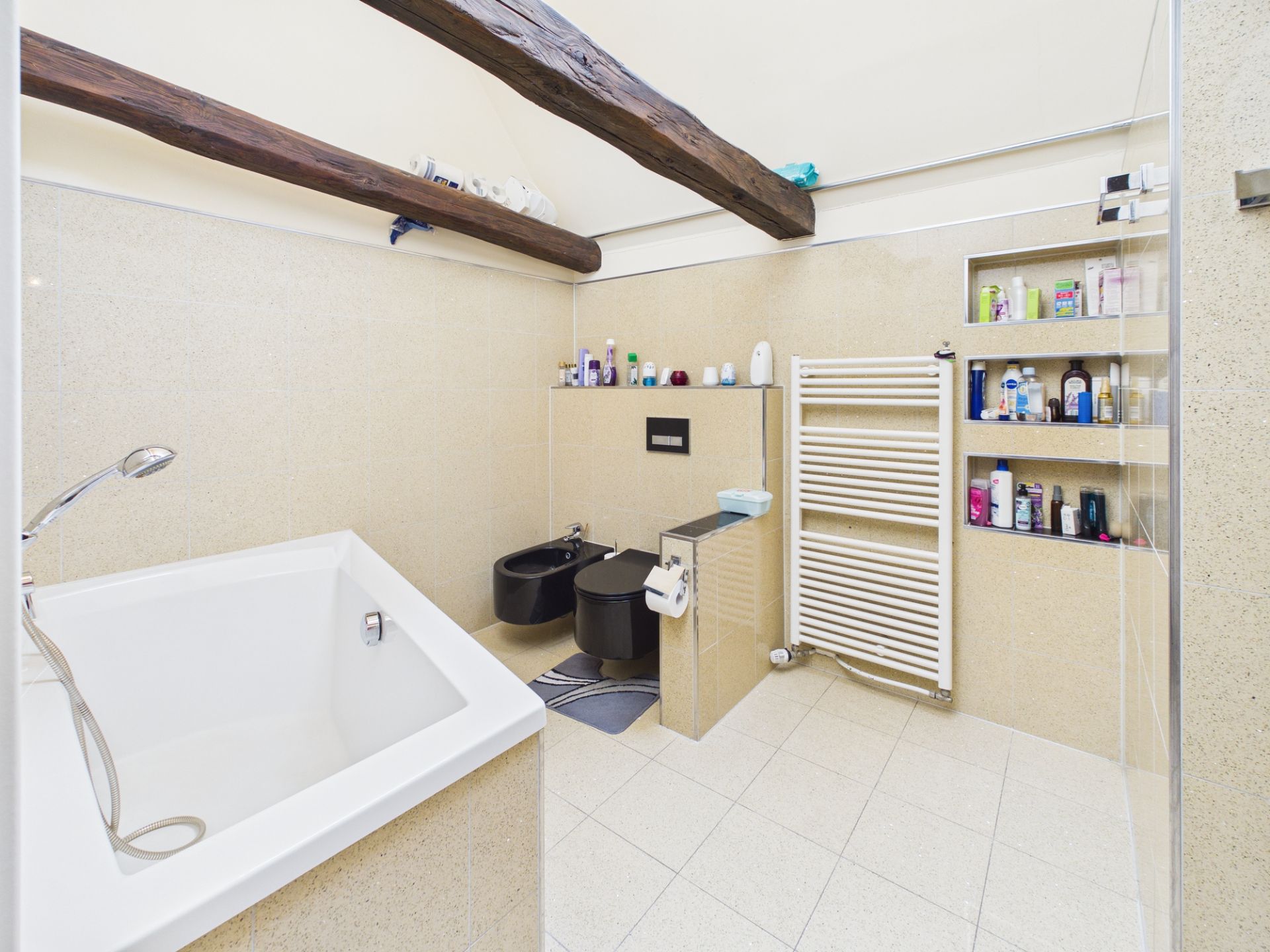 Modernes Badezimmer mit Badewanne, Bidet, WC, Handtuchheizkörper und Regalböden.