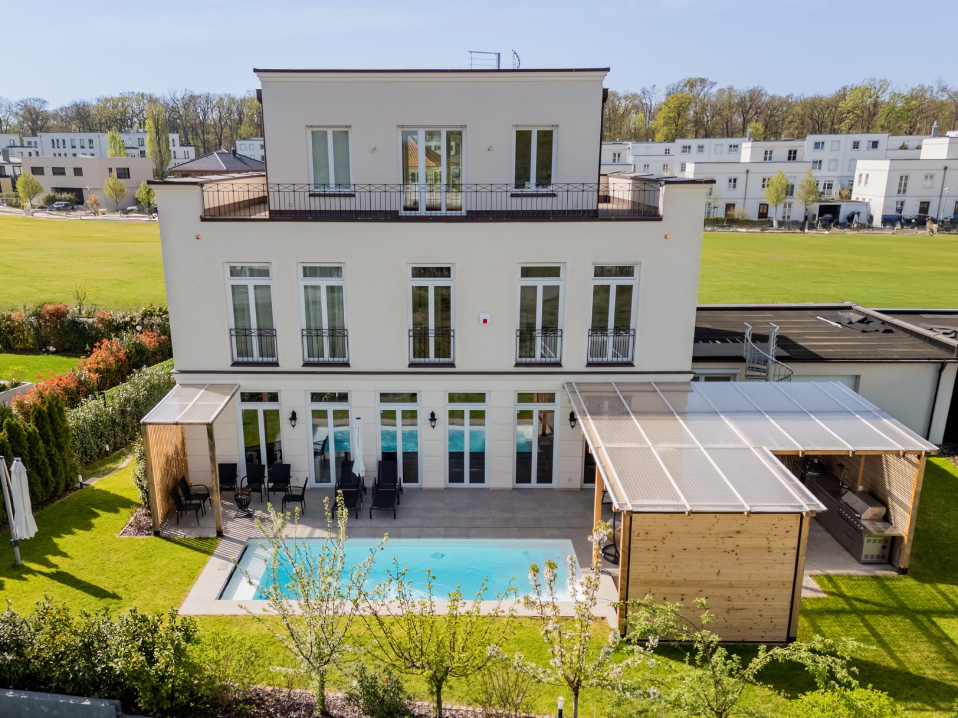 Modernes weißes Wohnhaus mit Terrasse, Pool und überdachtem Sitzbereich im Garten.