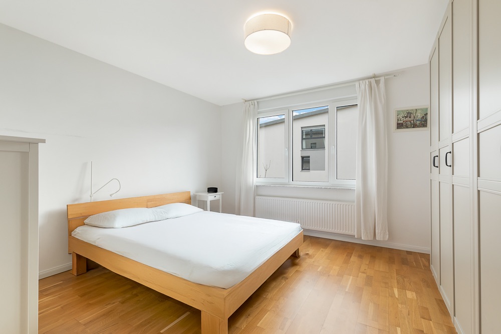 Helles Schlafzimmer mit Holzfußboden, Doppelbett, Fenster und Einbauschrank.