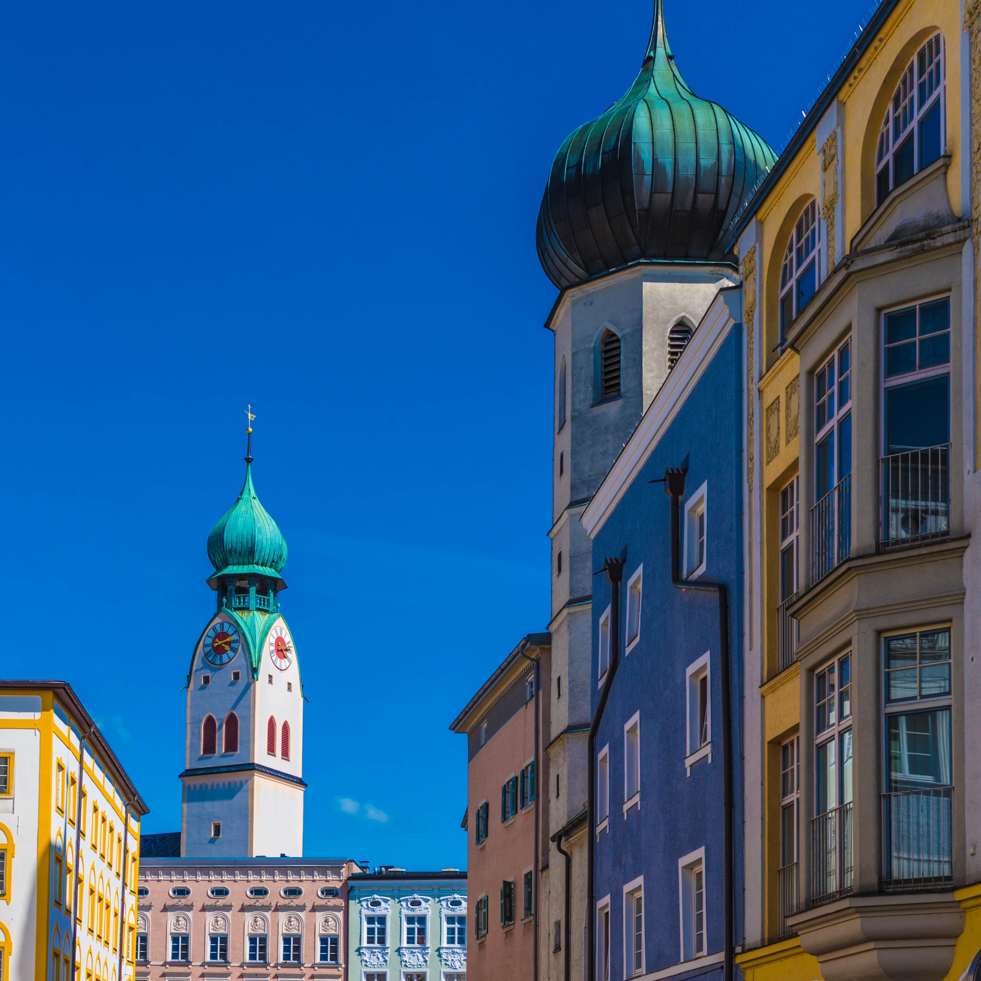 Bunte Wohngebäude und ein Kirchturm mit grüner Kuppel vor blauem Himmel.