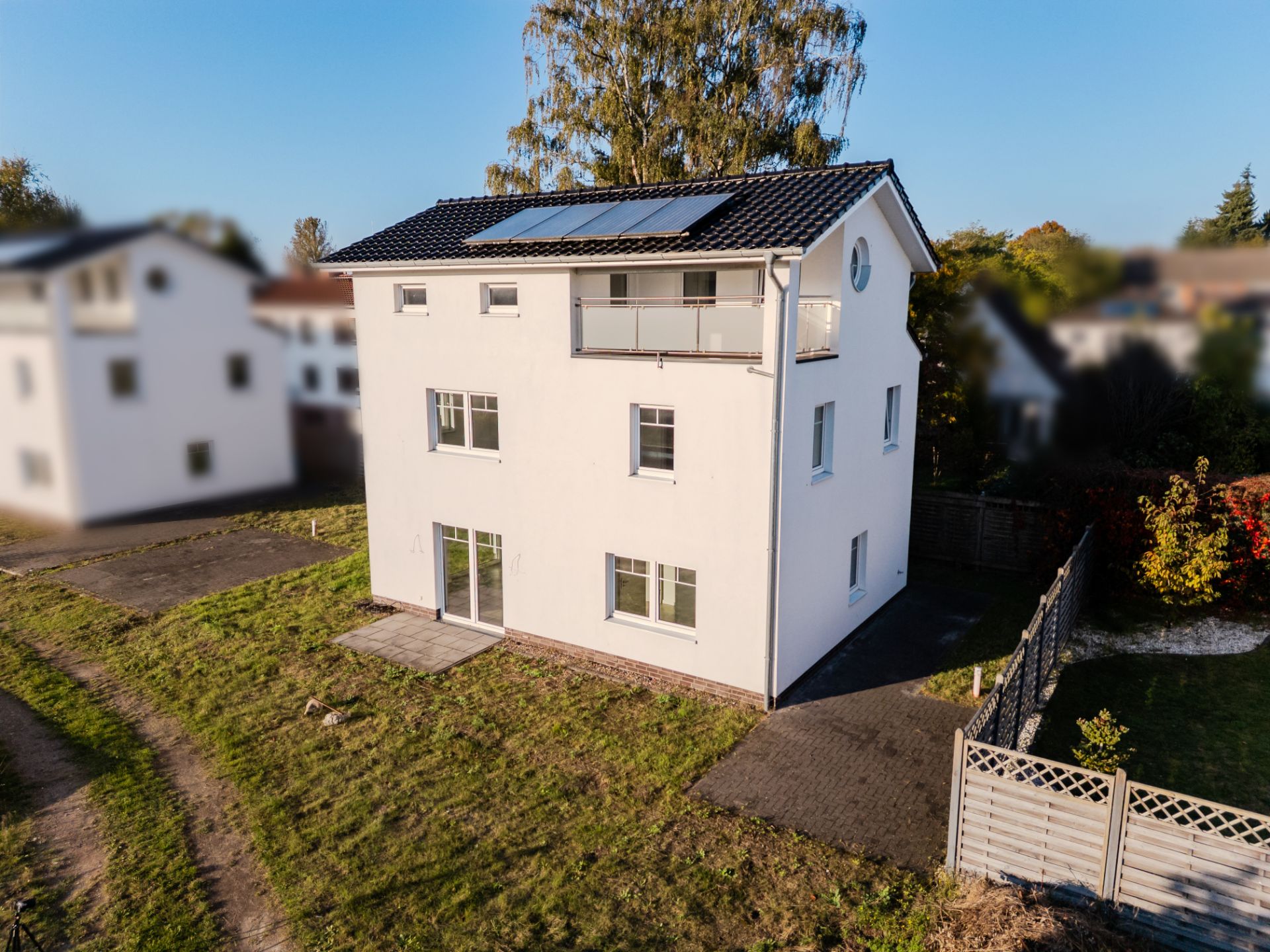 Modernes, weißes Einfamilienhaus mit Balkon, Garten und Solarpanelen auf dem Dach.